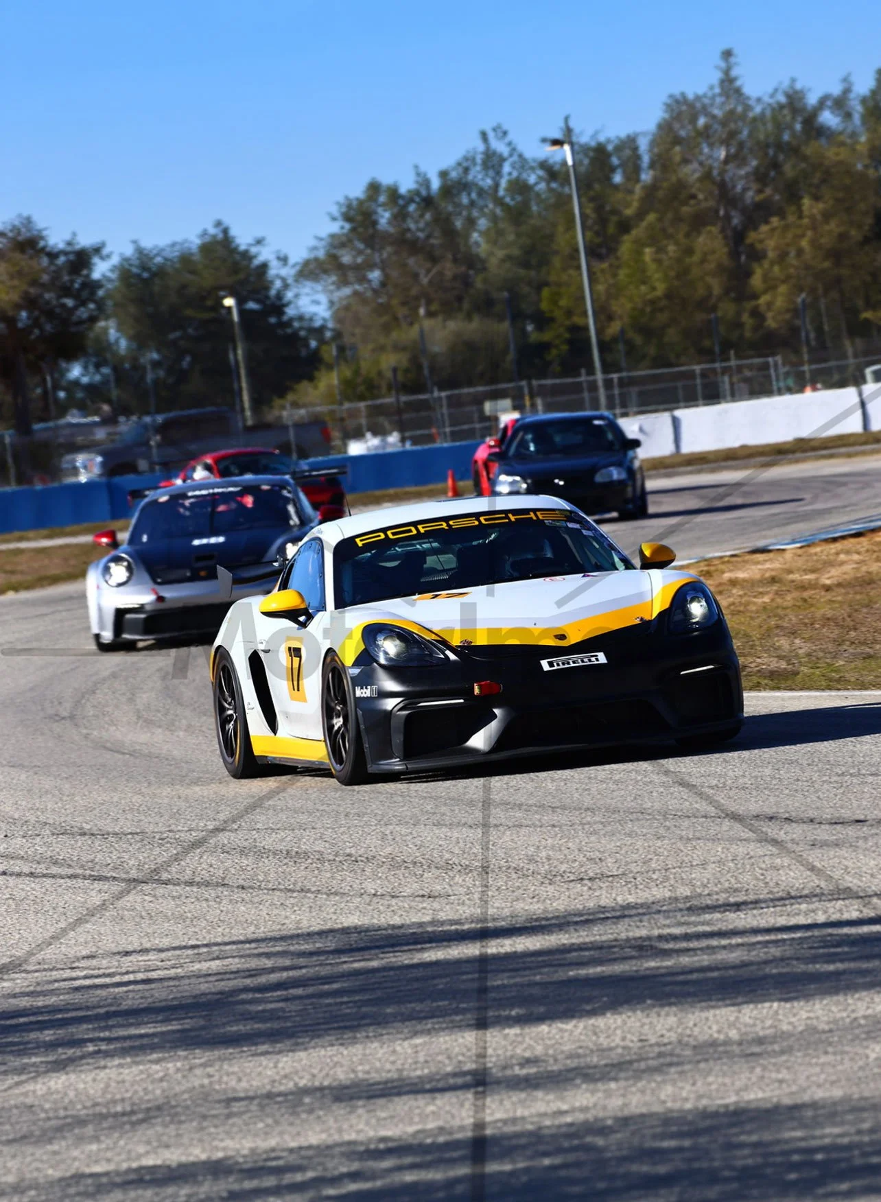 A white and yellow Porsche race car, number 17, on a racetrack, with other race cars in the background.