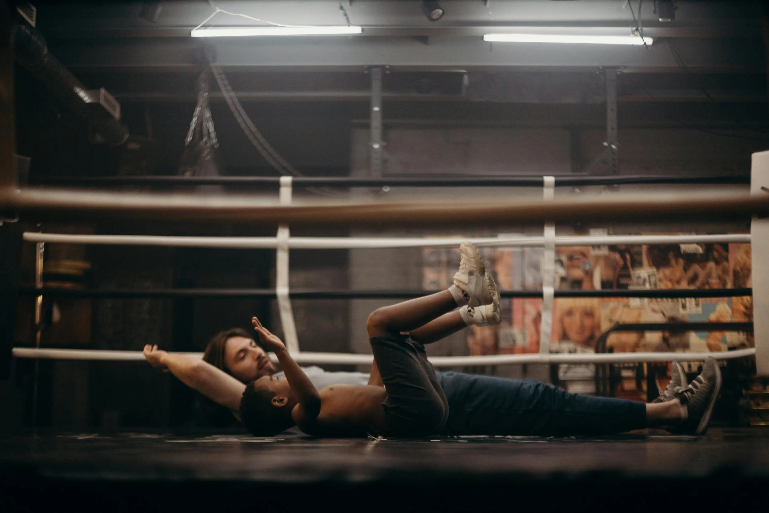 A young boy lying on the ground inside a boxing ring with a woman practicing boxing moves beside him.