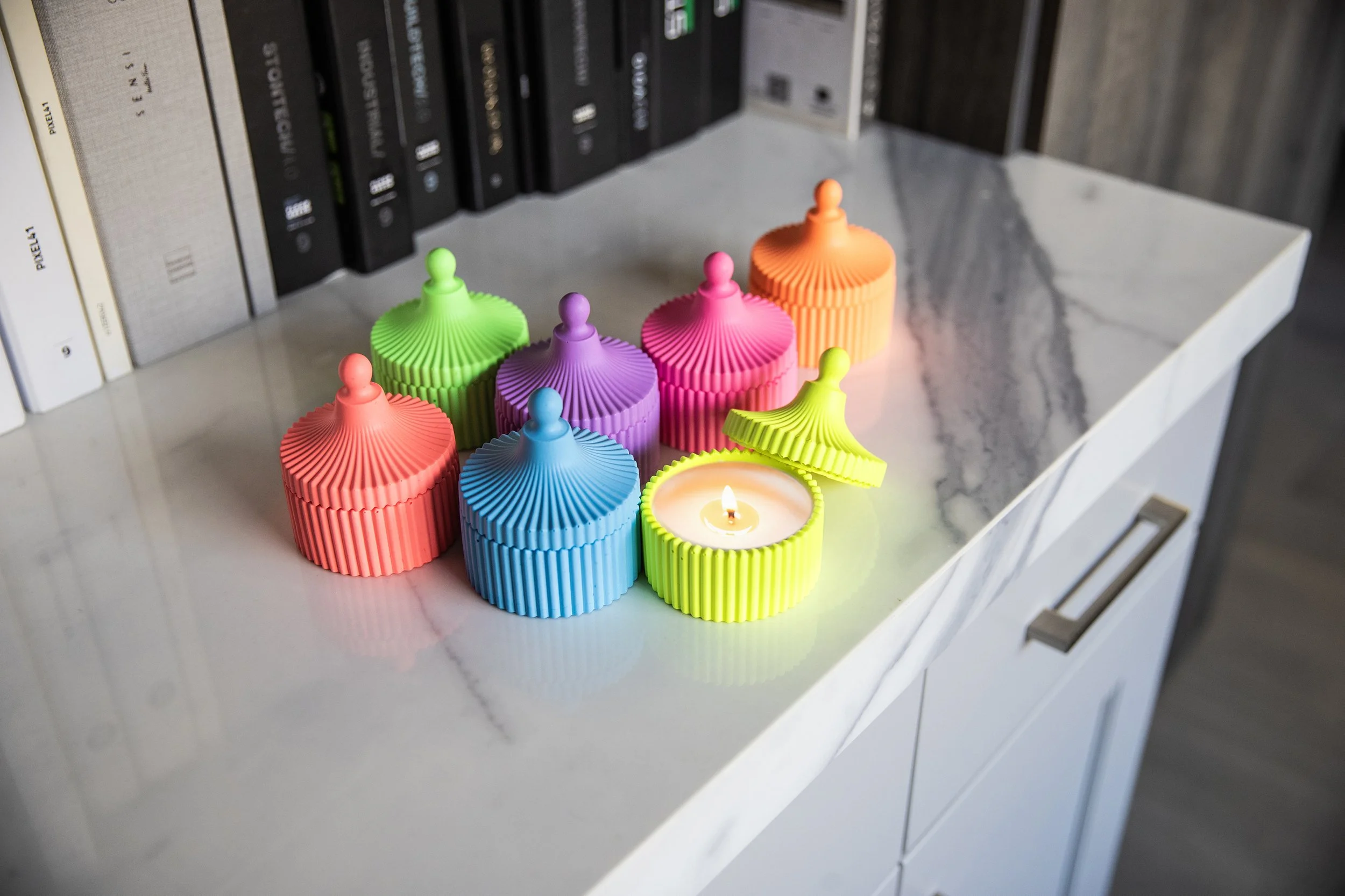 Colorful silicone cupcake-shaped candles arranged on a white marble surface with books in the background.