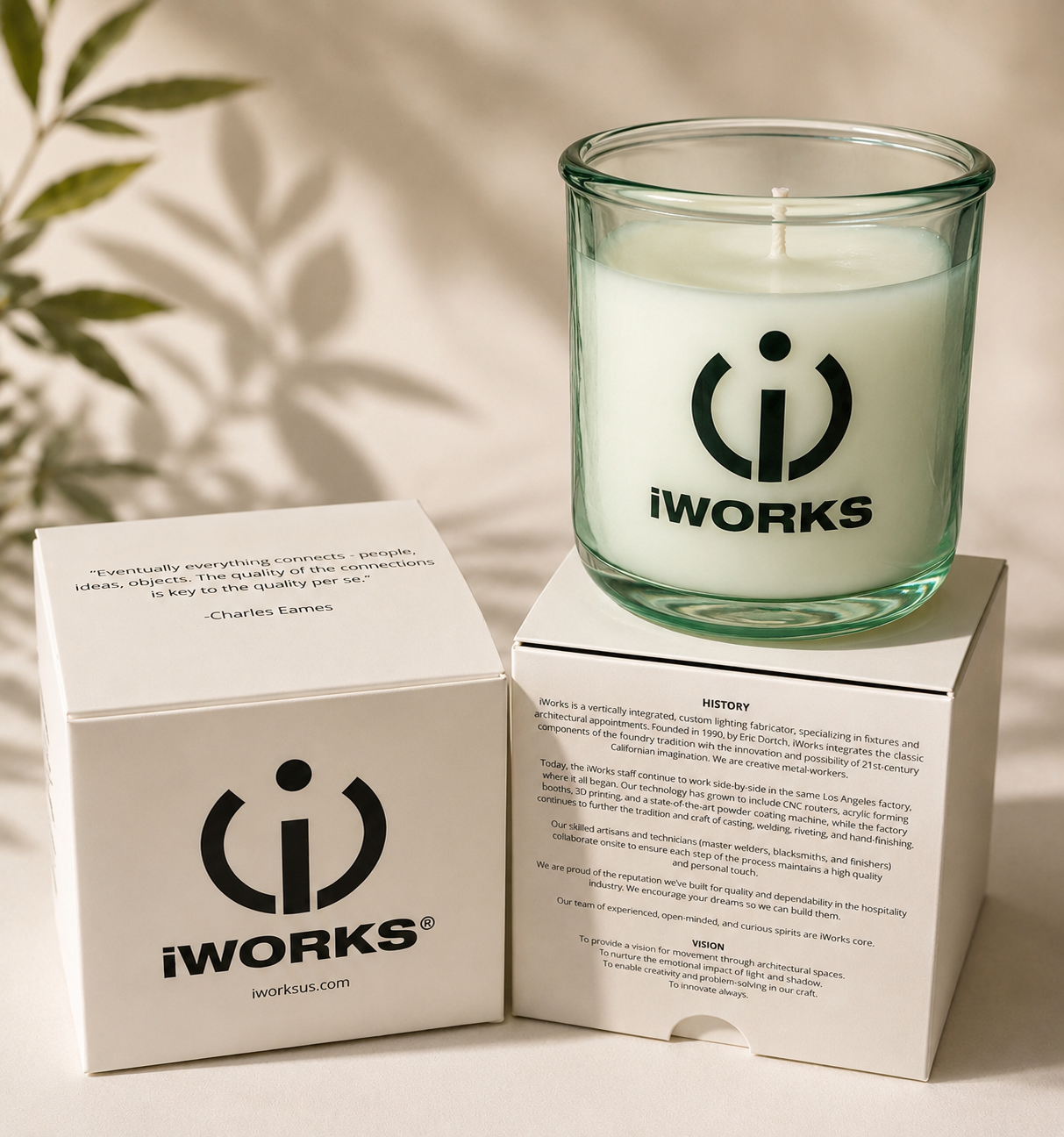 A white candle in a glass holder with the IWORKS logo, placed on top of a brochure and a white box with the same logo and text.