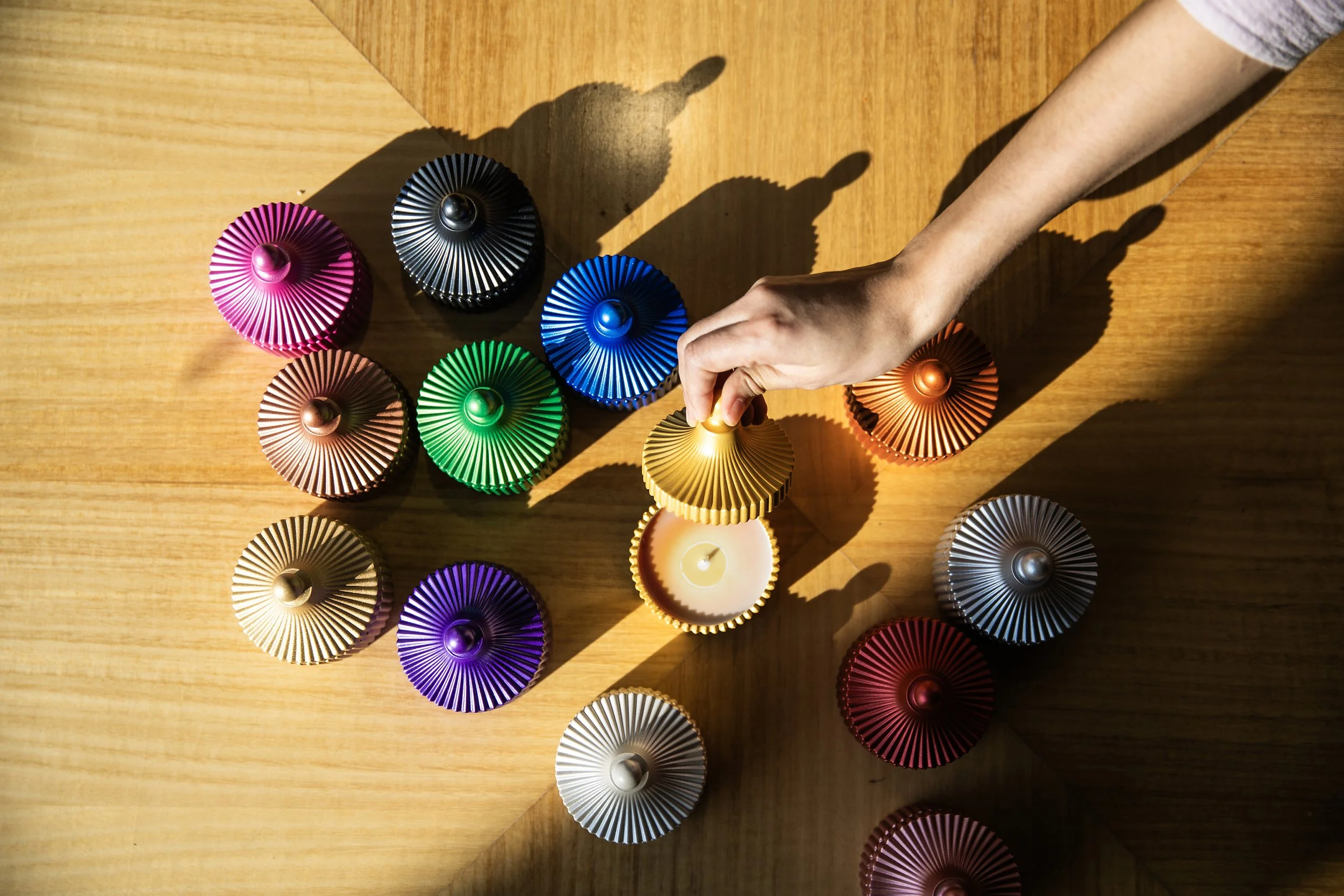 Colorful decorative candles arranged on a wooden surface with a hand lighting one of them.