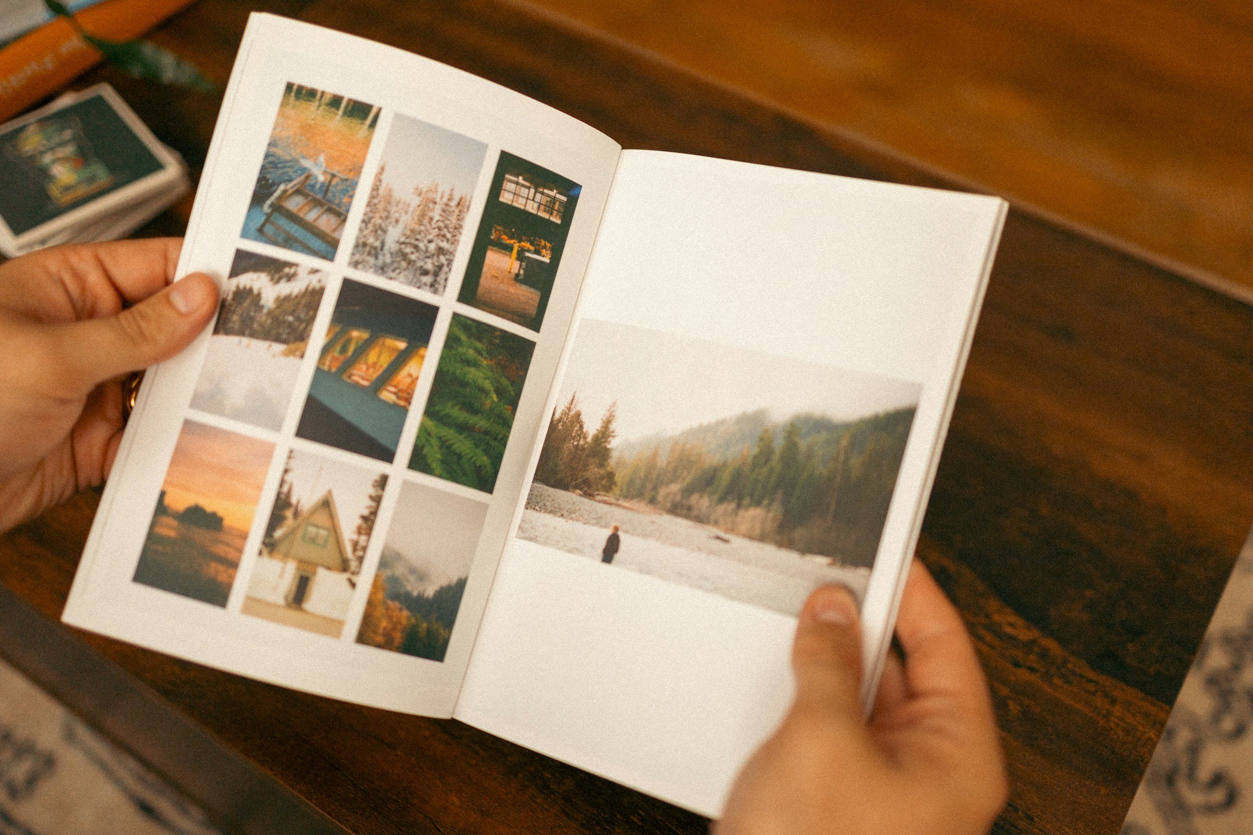 A person holding a photo album opened to a page with multiple pictures of outdoor landscapes, including trees, water, and a person standing by a river or lake.