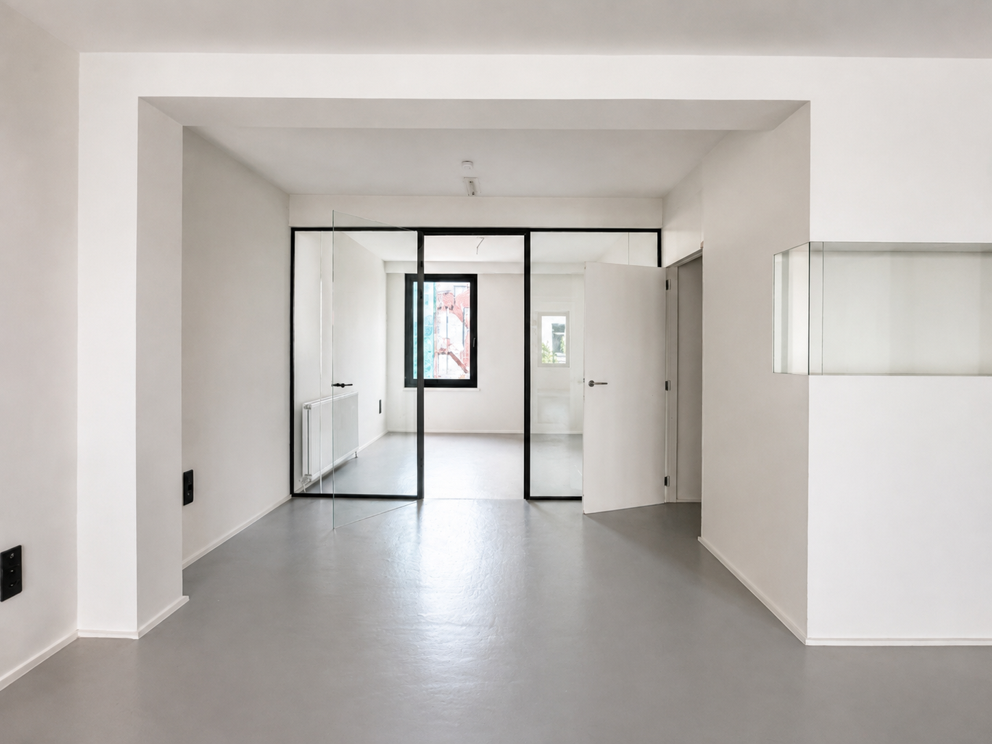 Modern office space with white walls, grey flooring and a black-framed glass door.