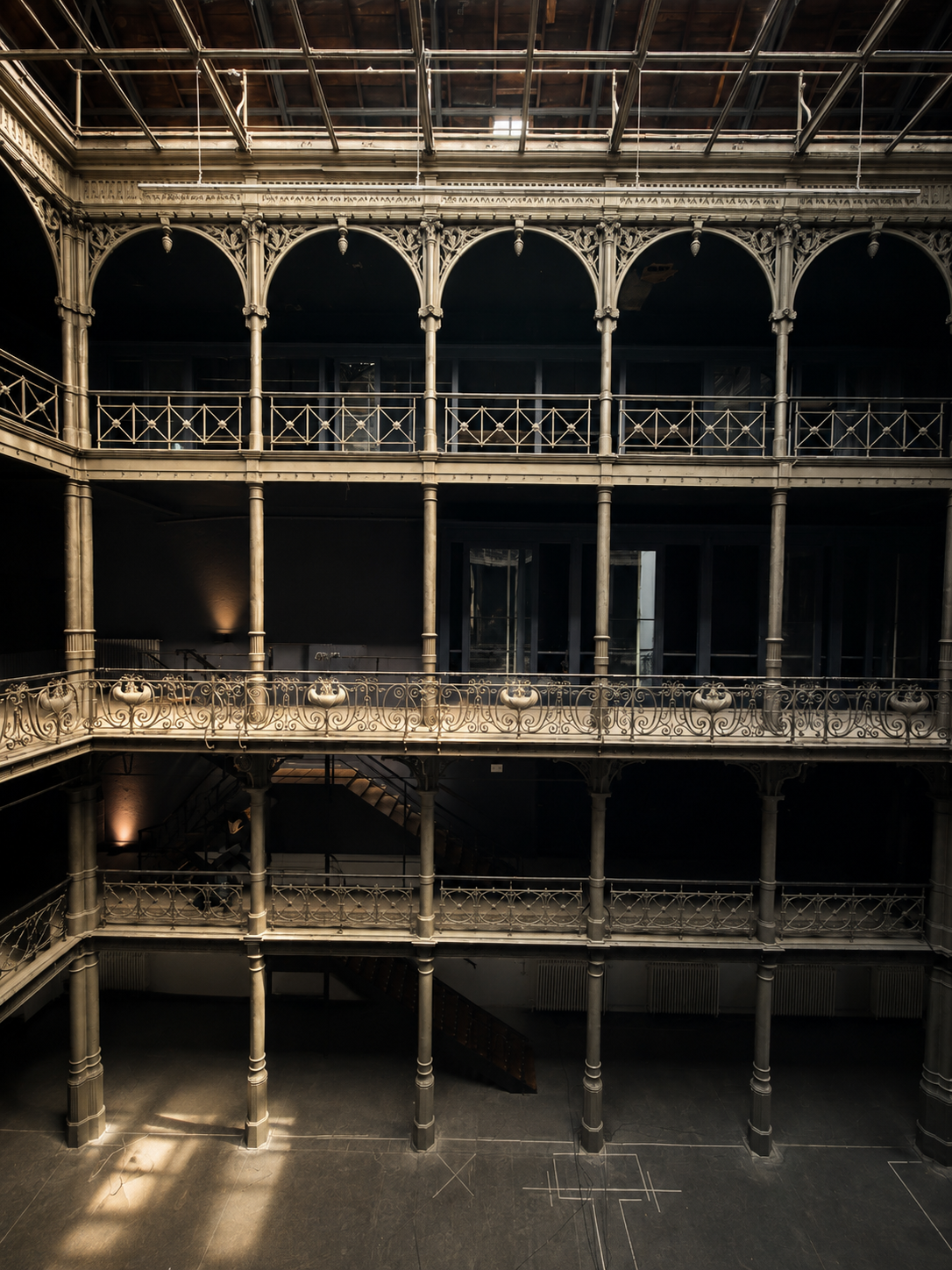 Interior view of an old multi-story building with ornate metal balconies and a glass roof, dimly lit with some sunlight.