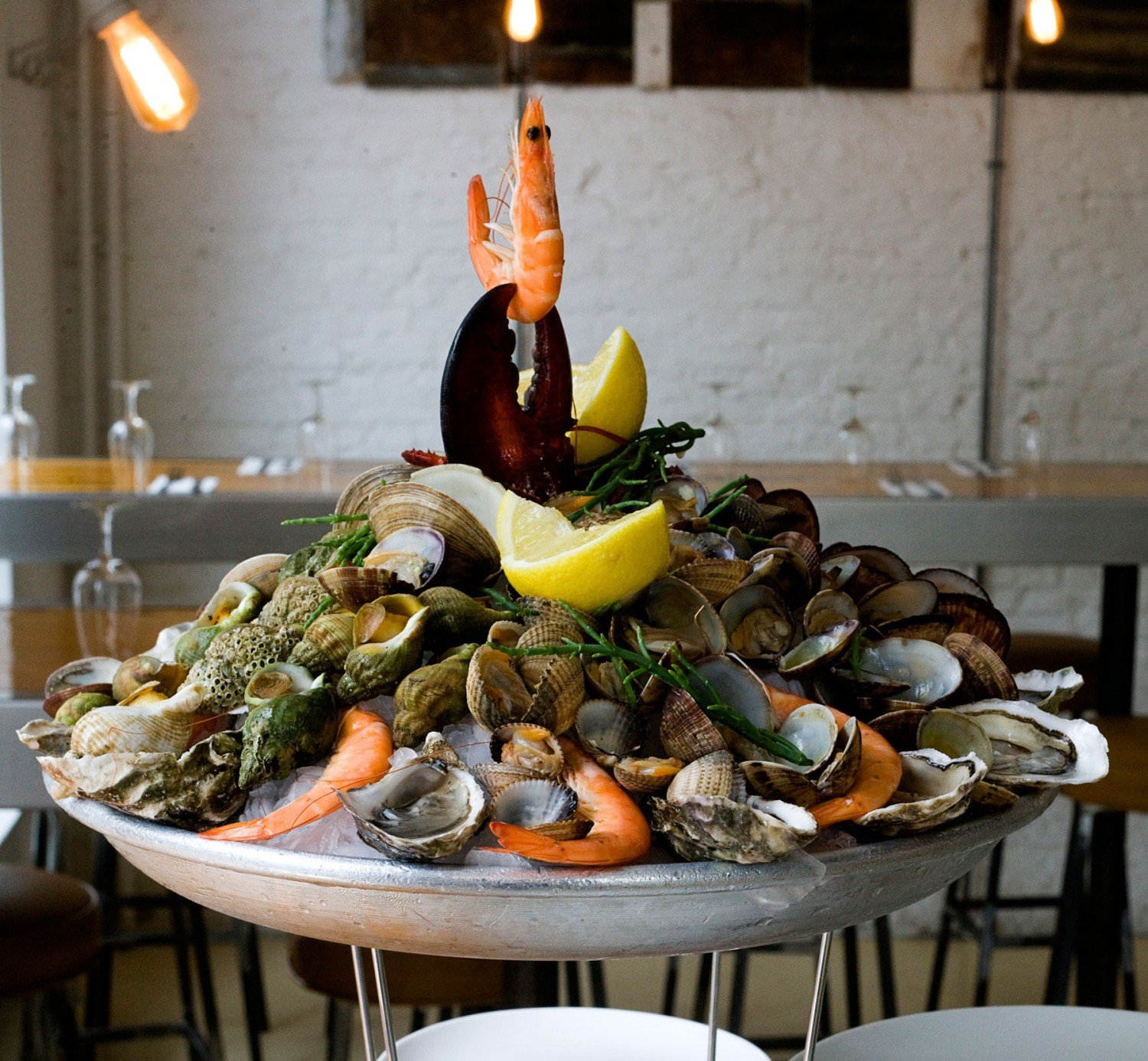 A seafood tower with shrimp, oysters, clams, and lemon wedges on ice, arranged decoratively in a restaurant setting.