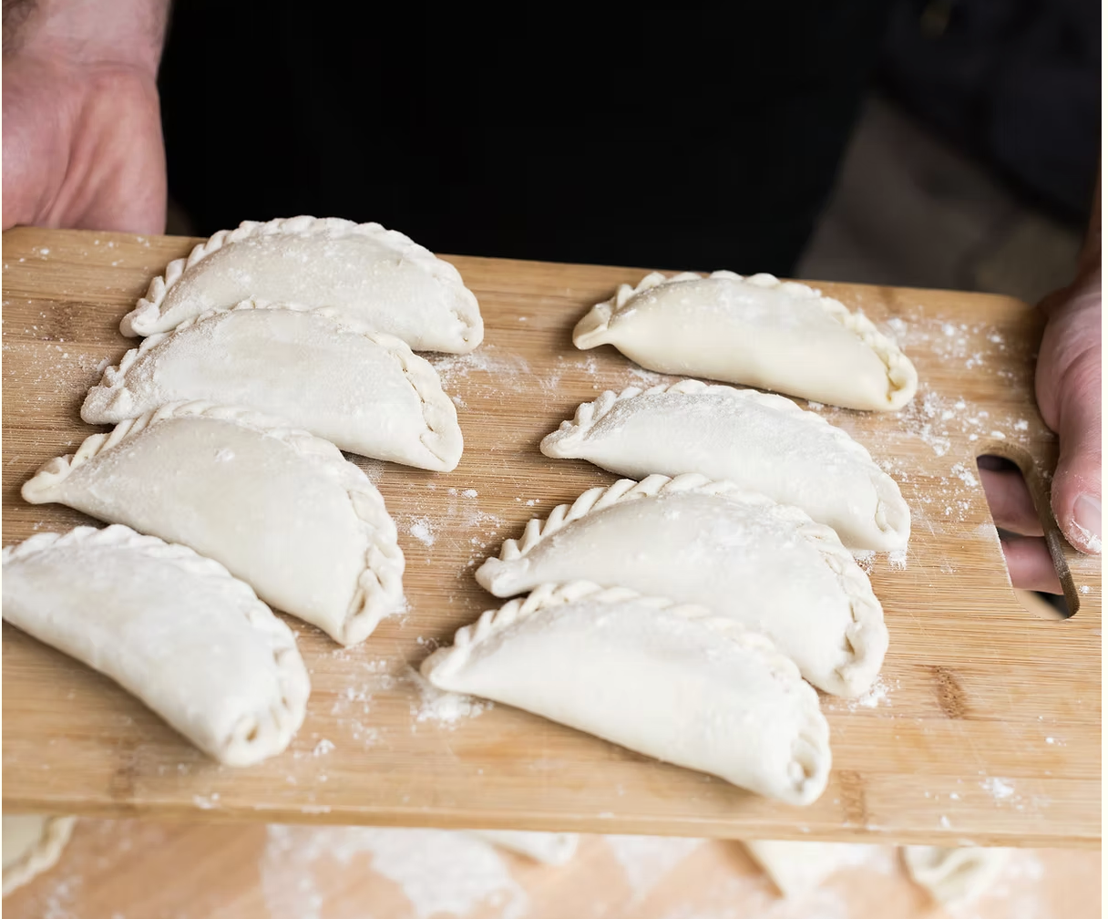 Uncooked dumplings arranged on a wooden cutting board with some flour sprinkled on top.