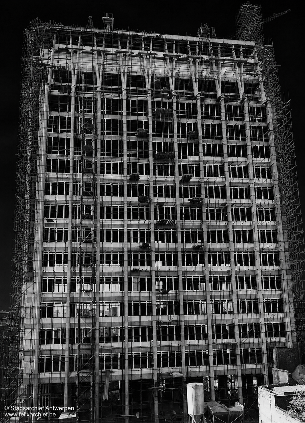 Black and white photo of a high-rise building under construction, surrounded by scaffolding, with many windows installed.