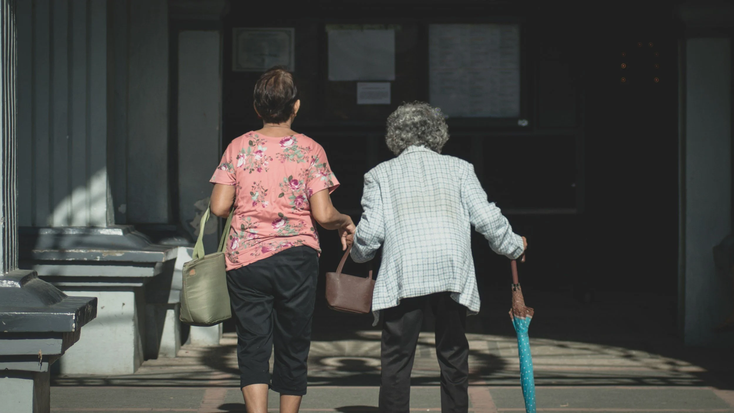 Two elderly women walking hand-in-hand, one using a cane, symbolizing compassionate caregiver support and connection in brain injury, brain tumor, and trauma counseling for survivors, caregivers, and healthcare professionals in Connecticut