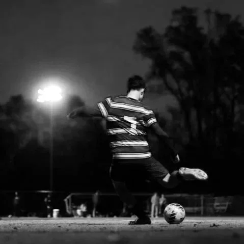 A person kicking a soccer ball on an outdoor field at night.