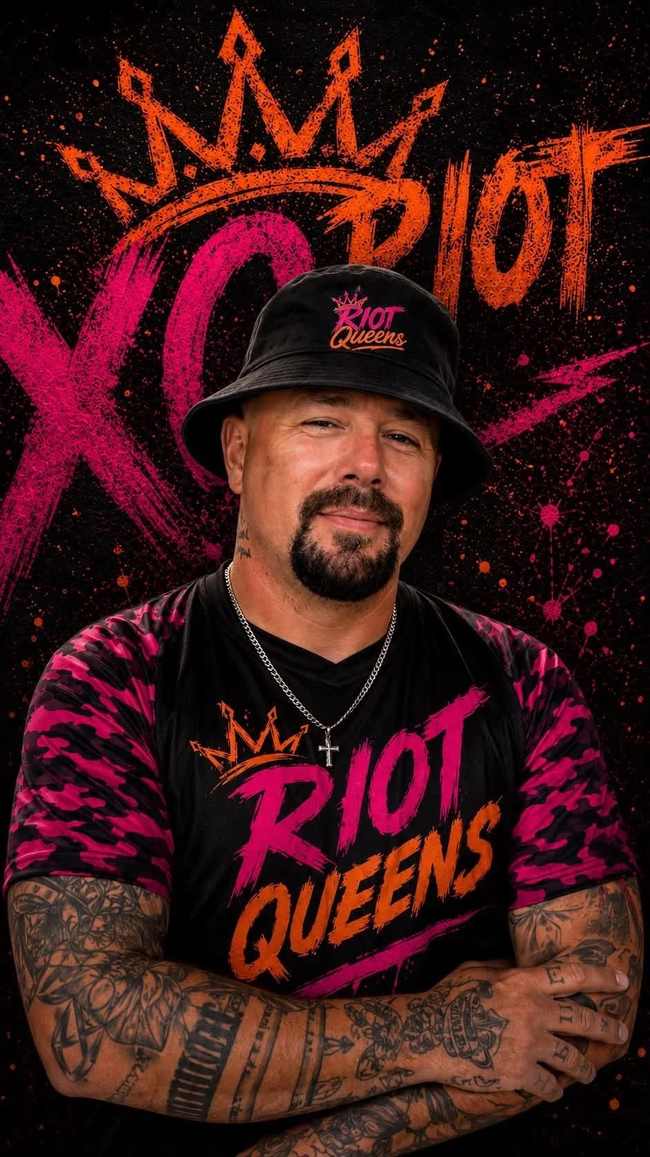A man with tattoos wearing a black bucket hat and a black and pink Riot Queens t-shirt, standing in front of a graffiti-style background with the words 'Riot Queens' and a crown graphic.