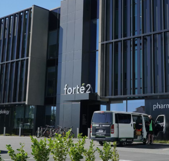 Modern office building with the sign 'forté2' and bicycles parked outside, with a van and a person near the entrance.