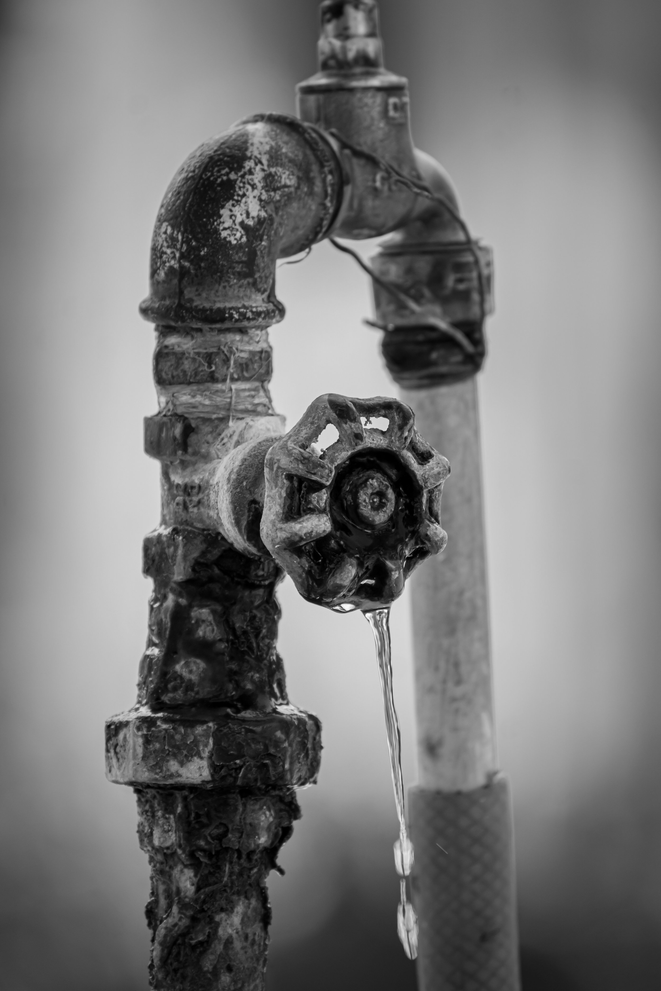 An old, rusted water pipe with a valve, leaking water. A stream of water is flowing down from the valve.