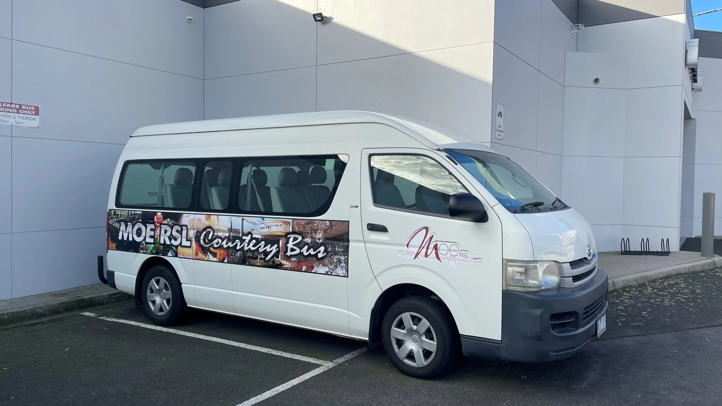 White bus with signage for Moe RSL Courtesy Bus parked in a parking lot next to a white building
