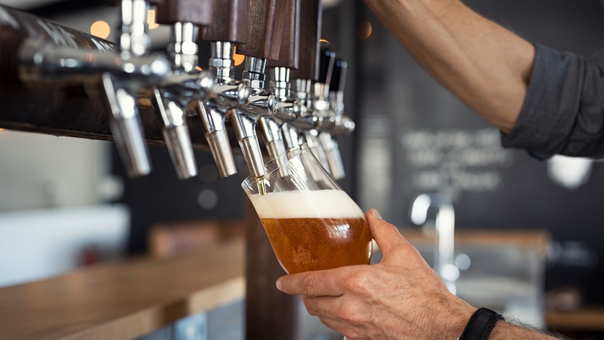 A person is filling a glass of beer from a tap at a bar or brewery.