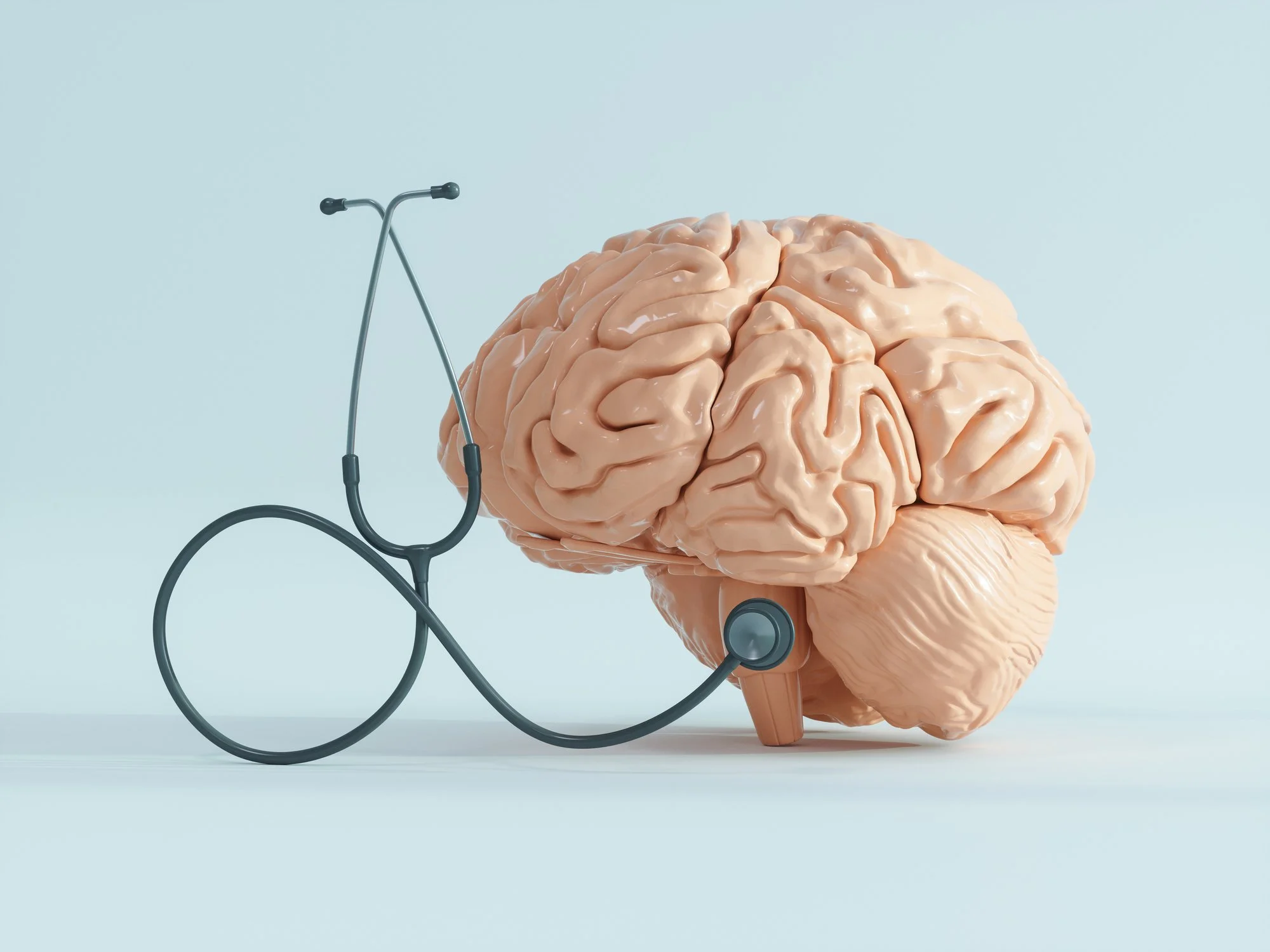 A realistic model of a human brain with a stethoscope draped around it, symbolizing medical or mental health care, set against a plain blue background.