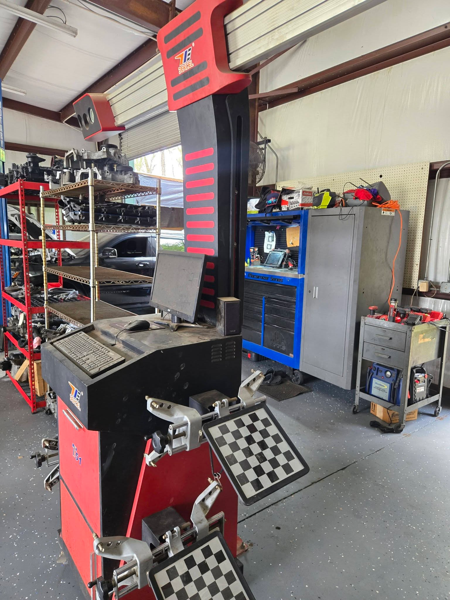 Garage with a wheel alignment machine, a computer, tools, and car parts on shelves.