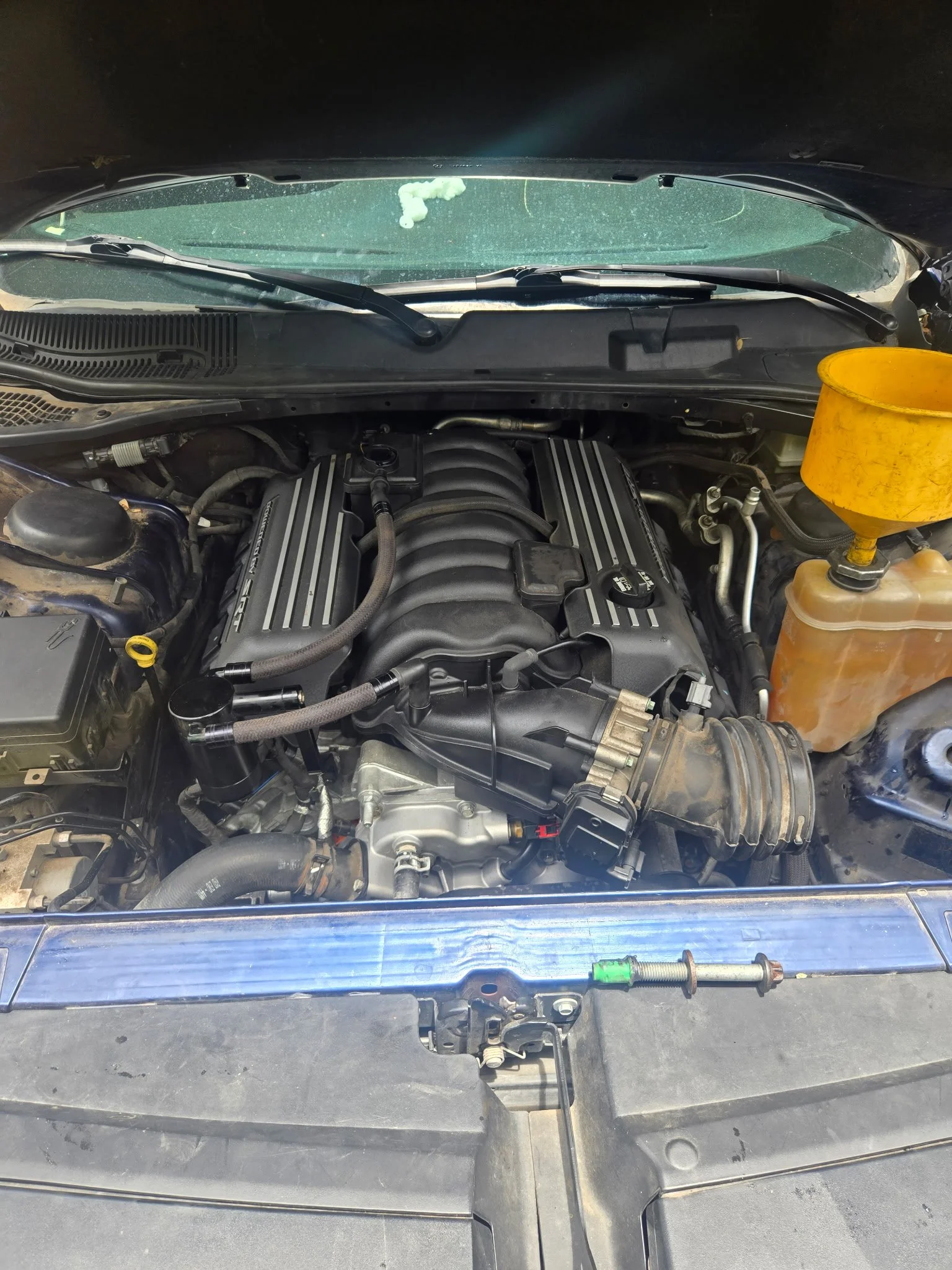 View of a car engine bay with various engine parts and a yellow coolant reservoir on the right side.