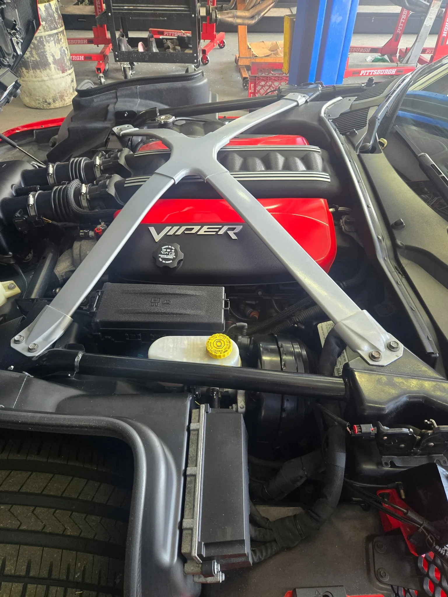 Engine bay of a sports car with a red intake cover marked 'Viper' and various components, tools, and car repair equipment around.