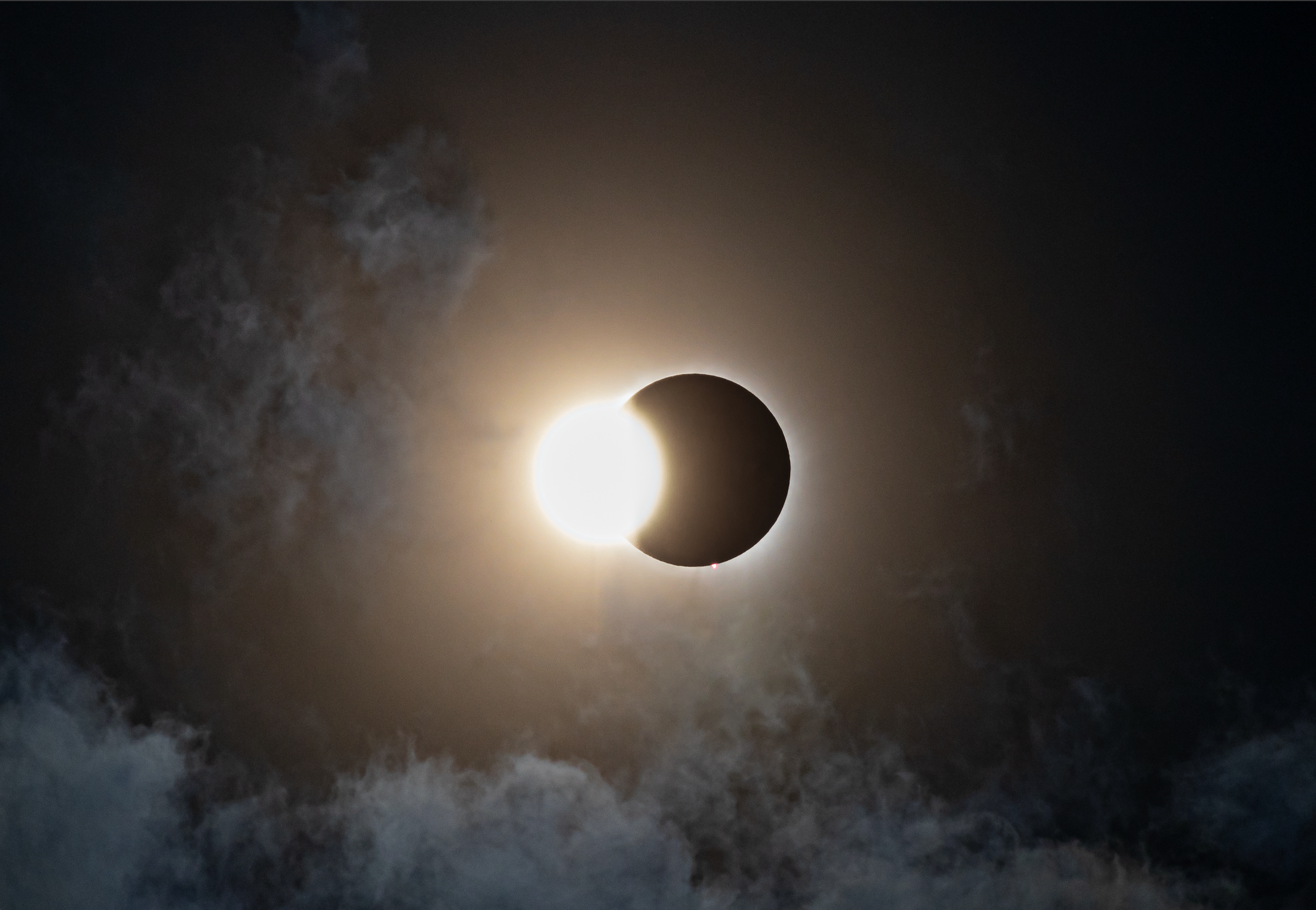 A solar eclipse where the moon covers the sun, with a bright halo and wispy clouds in the background.