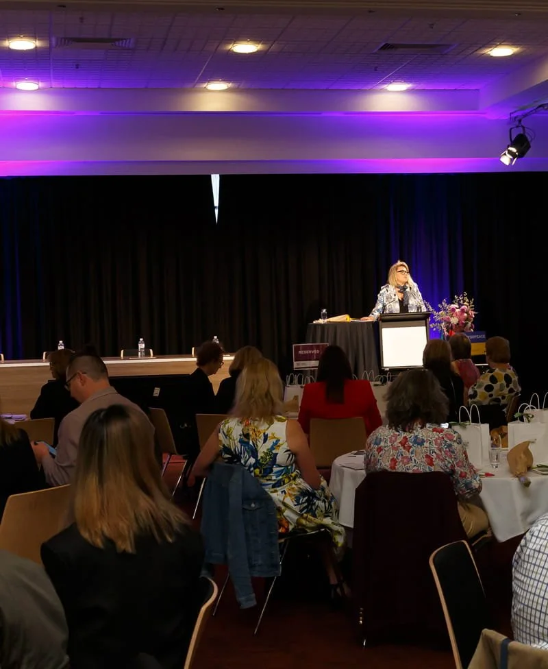 Kylie Ward speaking at a podium at an event with people seated at tables