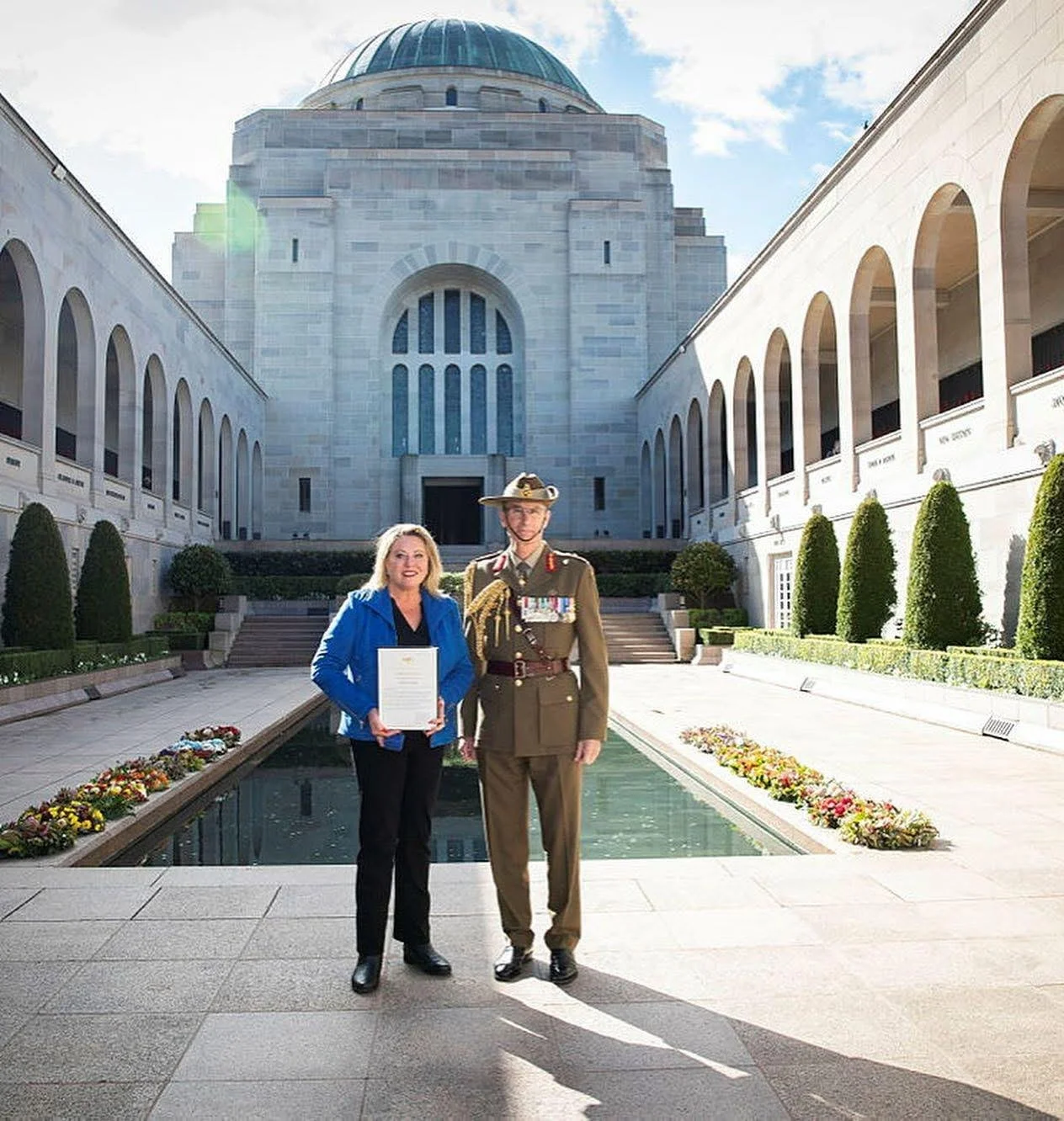 Kylie Ward stands with General Angus Campbell at the Australian War Memorial in Canberra, holding a Certificate of Commendation, with the Hall of Memory and reflection pool in the background.