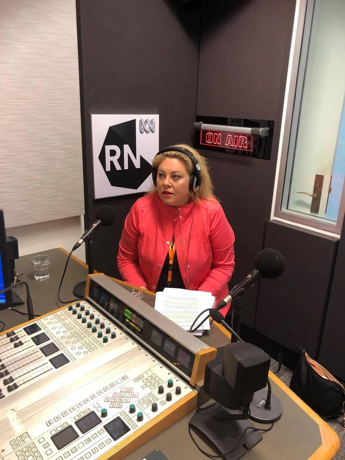 Kylie Ward wearing headphones in a radio studio, speaking into a microphone during an ABC Radio National on air segment.