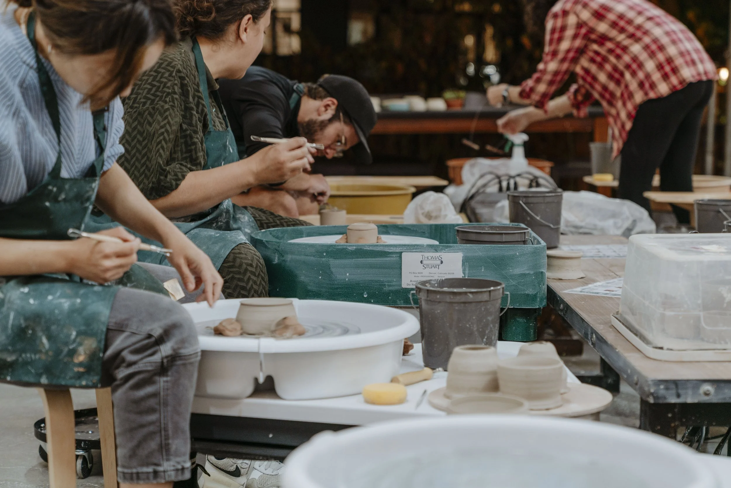 People working on pottery projects at a pottery workshop, with various pottery tools and clay on tables.
