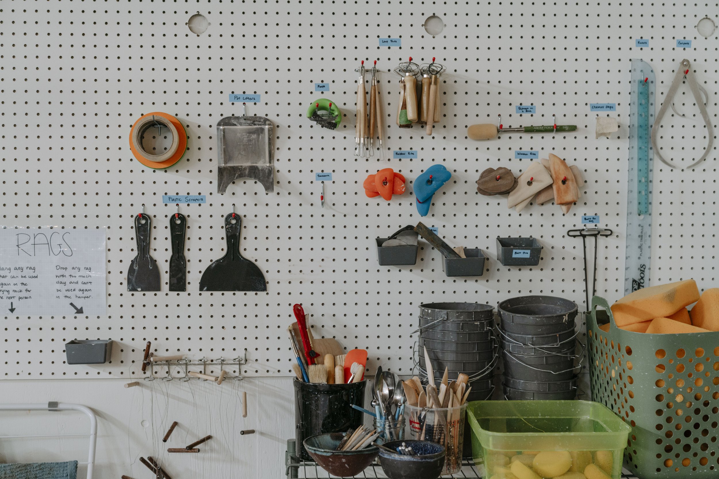 A white pegboard with various hand tools hanging, including wrenches, pliers, screwdrivers, and a hammer, mounted on a perforated metal wall.