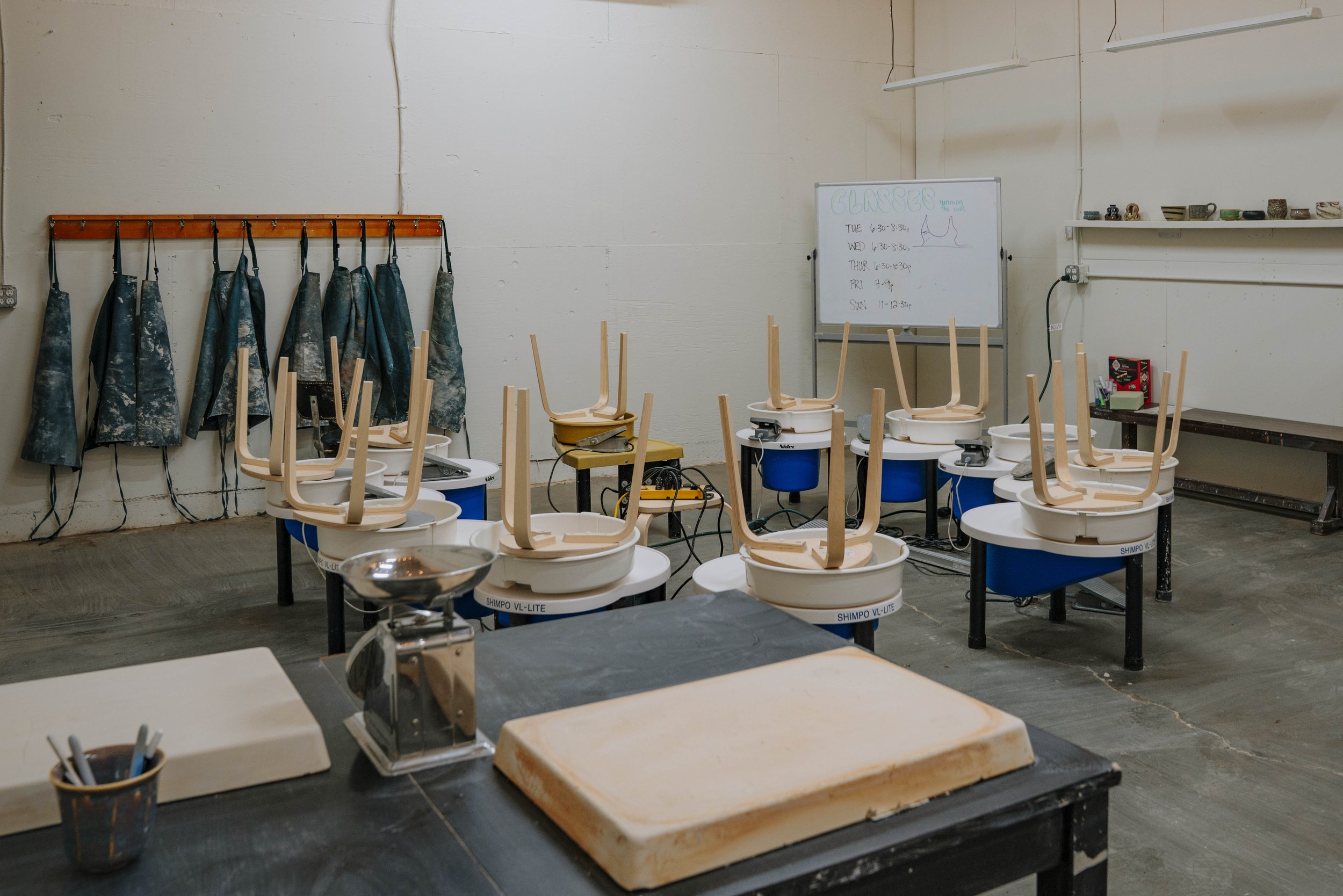 Classroom with pottery wheels, a work table, aprons, and a whiteboard 