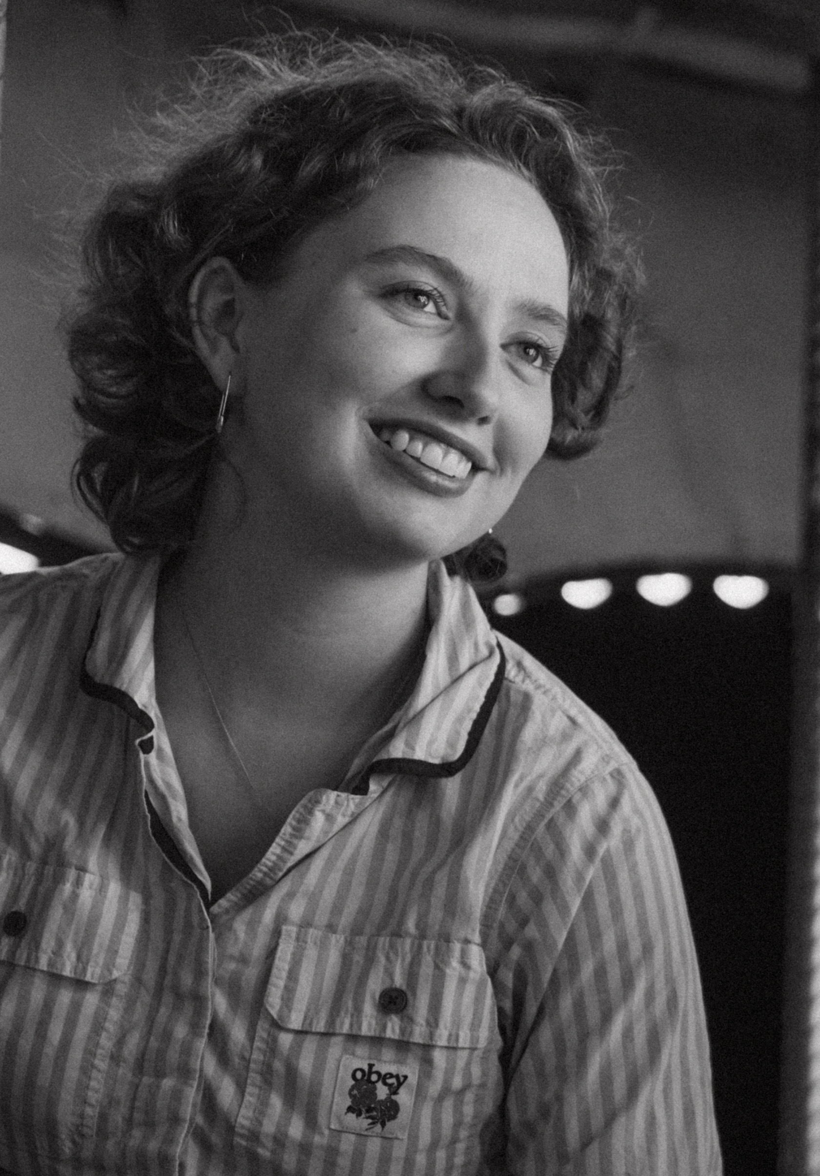 Black and white photo of a smiling woman with curly hair, wearing a striped shirt.
