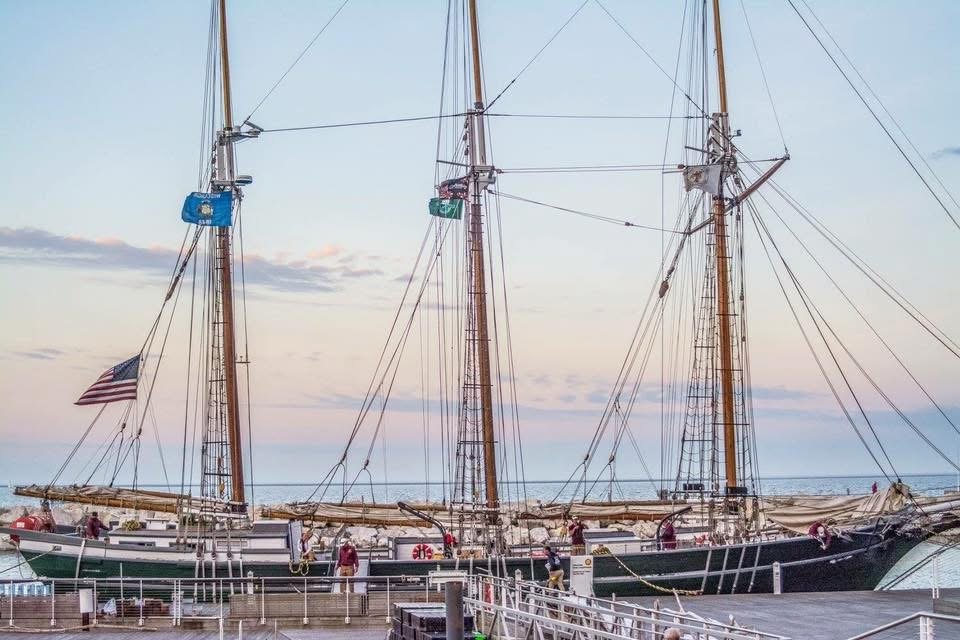 Photograph by Ashley Whitt of a historic tall ship docked at a Wisconsin pier on Lake Michigan during sunset, with calm water, towering masts, and a pastel evening sky.