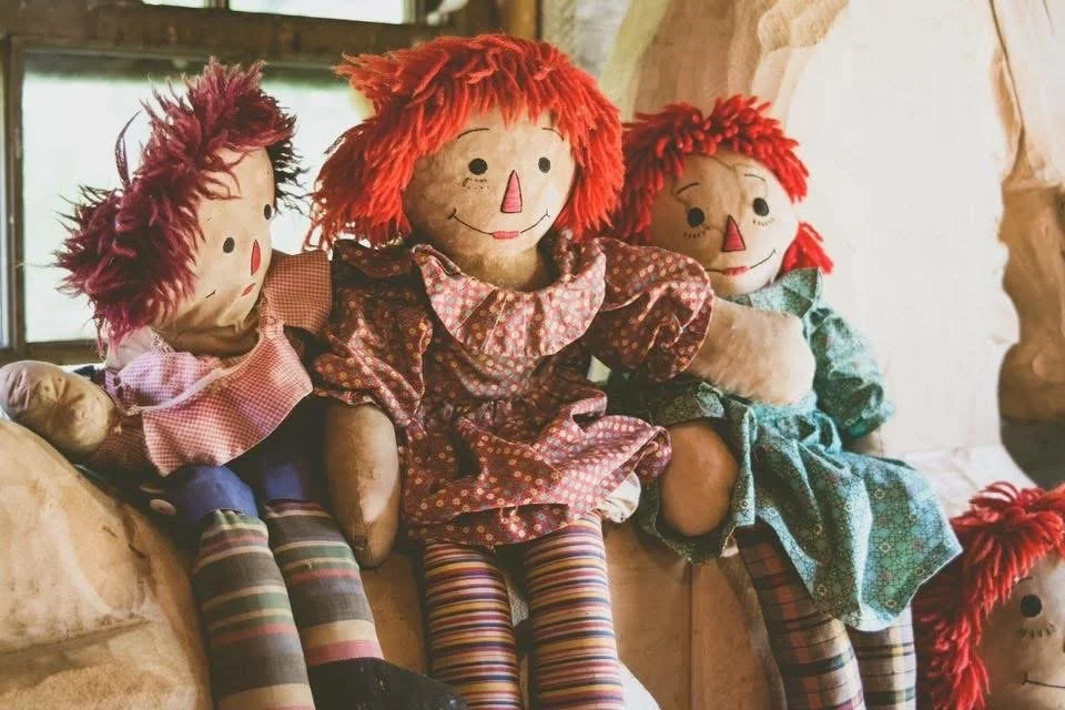 Photograph by Ashley Whitt of three vintage rag dolls with bright red yarn hair, colorful patchwork dresses, and striped stockings, displayed at Hippie Tom's Serendipity Farm in Waterford, Wisconsin.