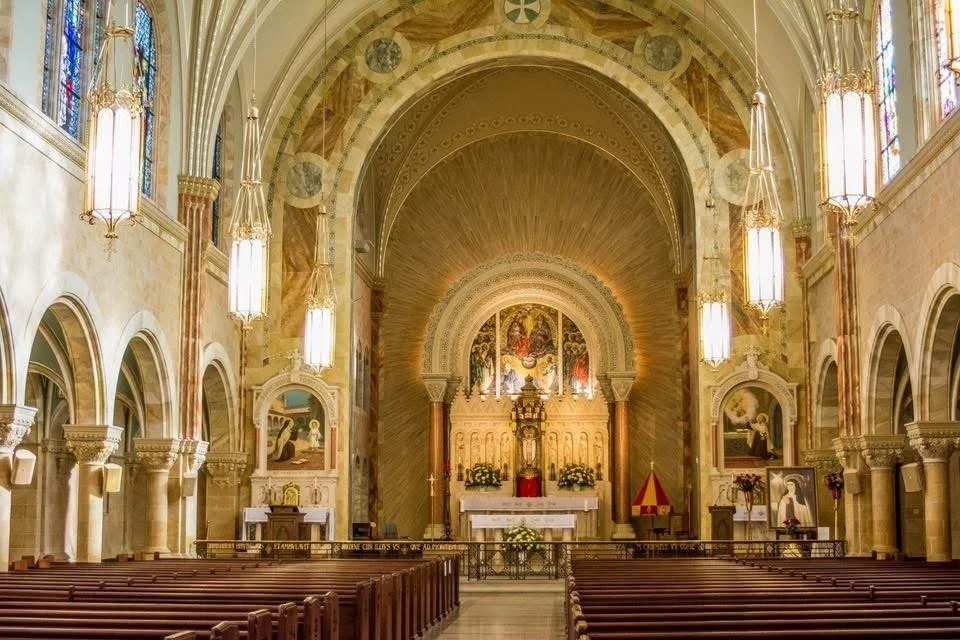 Photograph by Ashley Whitt of the interior of the Basilica at Holy Hill National Shrine of Mary, Help of Christians in Hubertus, Wisconsin, featuring an ornate altar, stained glass windows, soaring arches, and rows of wooden pews.