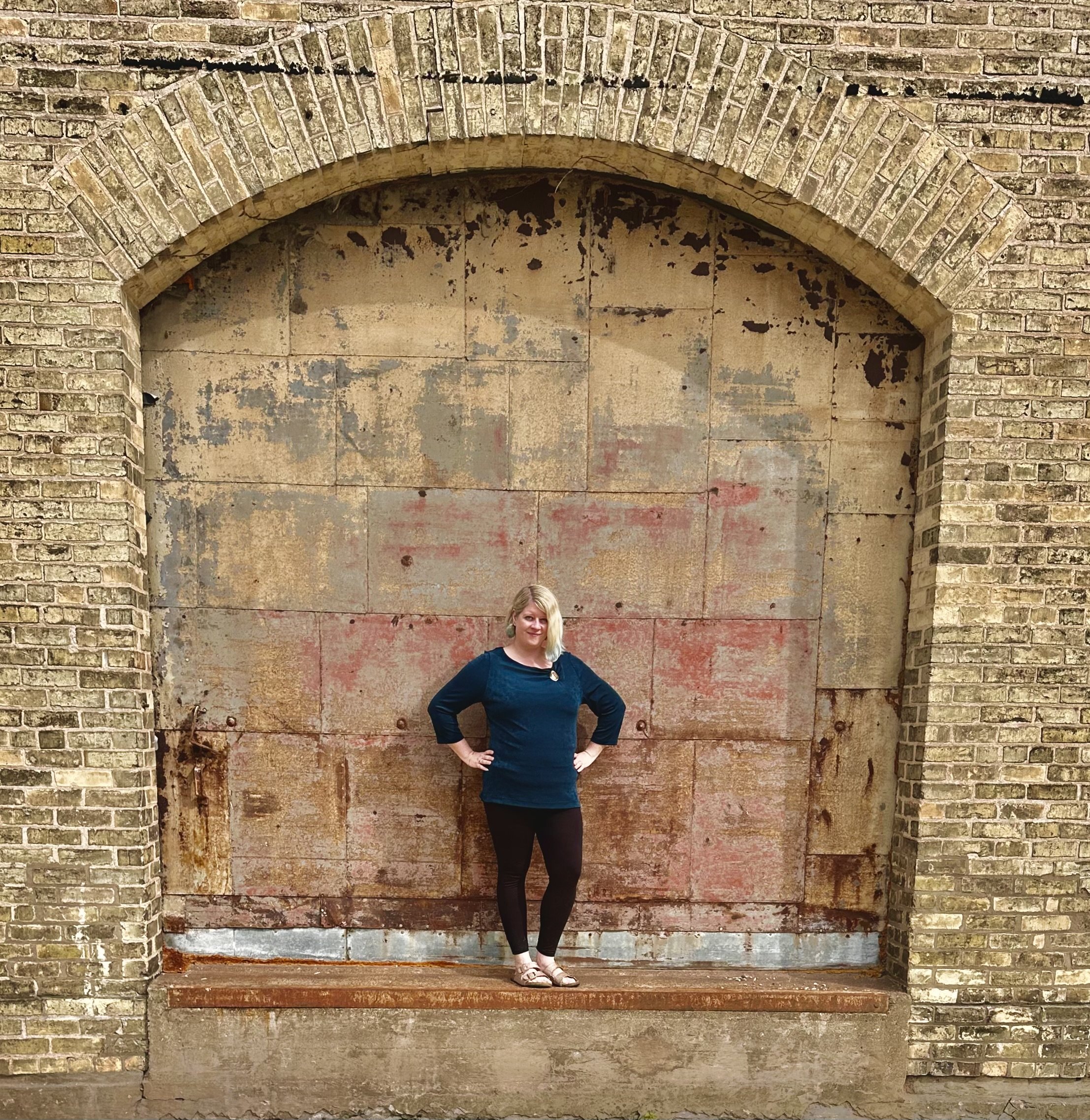 Ashley Whitt standing beneath a historic brick and metal archway at the Horlick Malted Milk Company, smiling with hands on her hips.