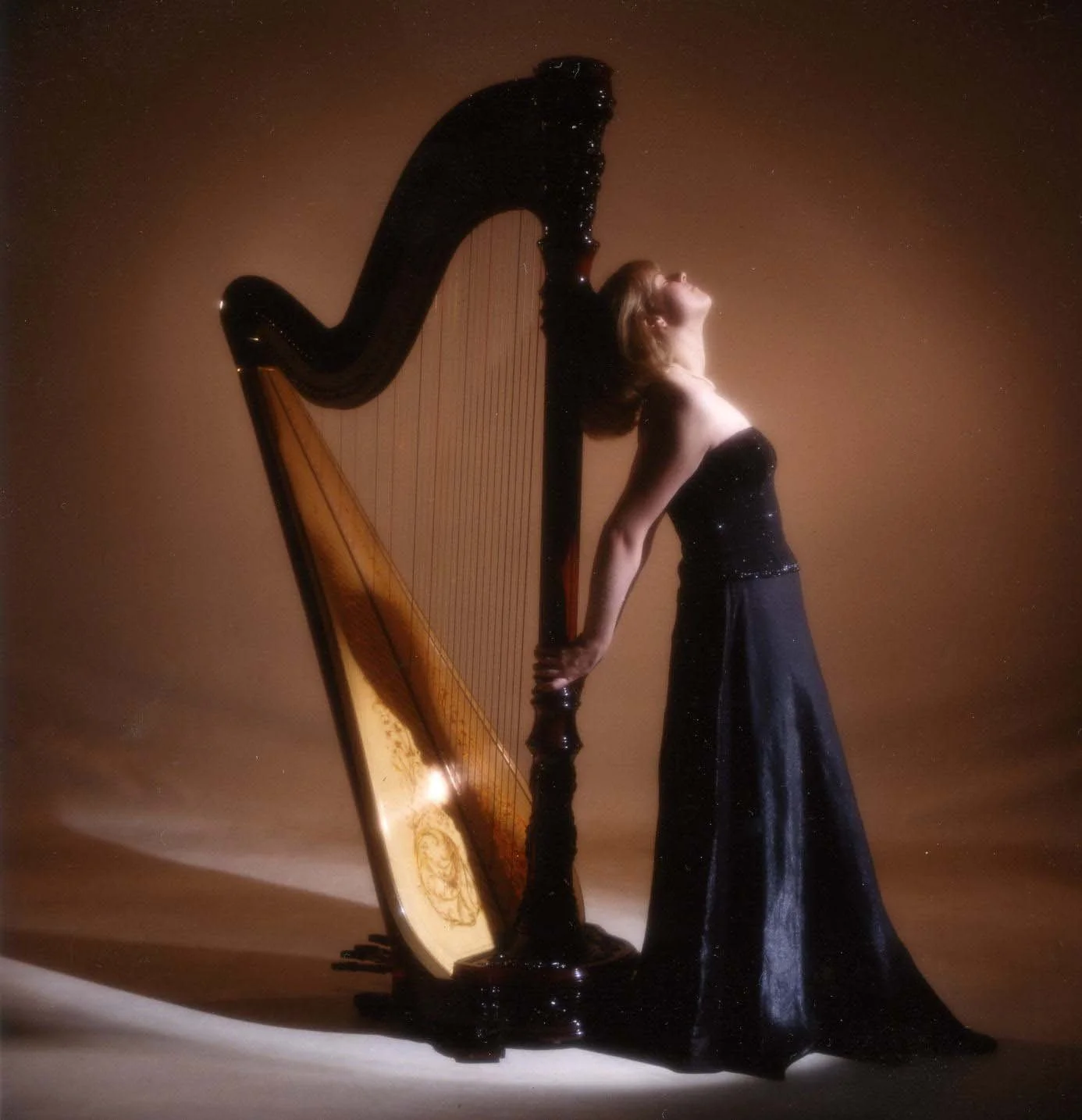 Ashley Whitt standing beside a concert harp in a black gown, eyes closed in a quiet, reflective portrait representing her lifelong connection to music.