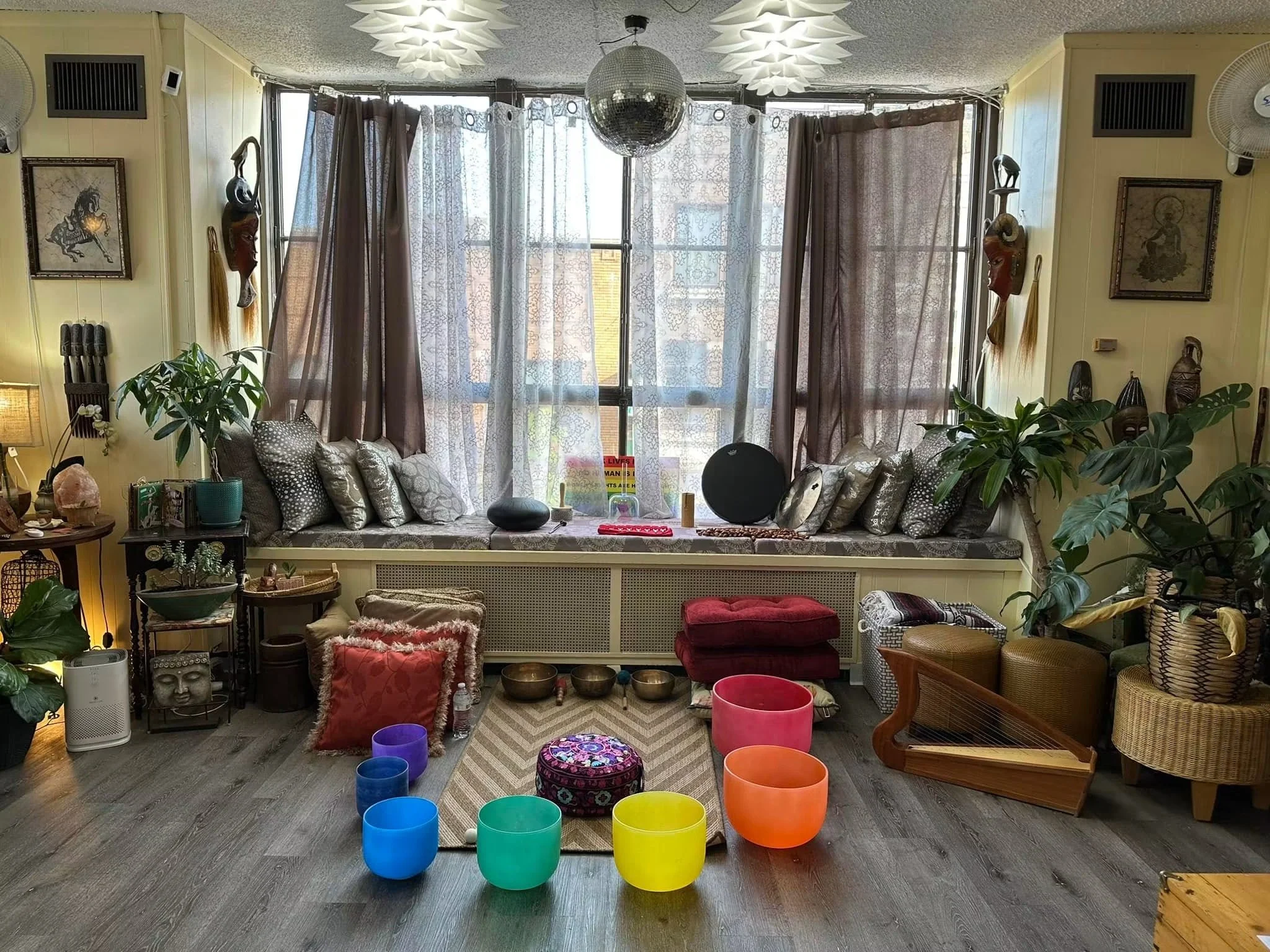 Sound healing and meditation space featuring colorful crystal singing bowls and other sound healing instruments arranged on a rug, surrounded by plants, comfortable seating, and calming décor designed for relaxation and mindfulness.