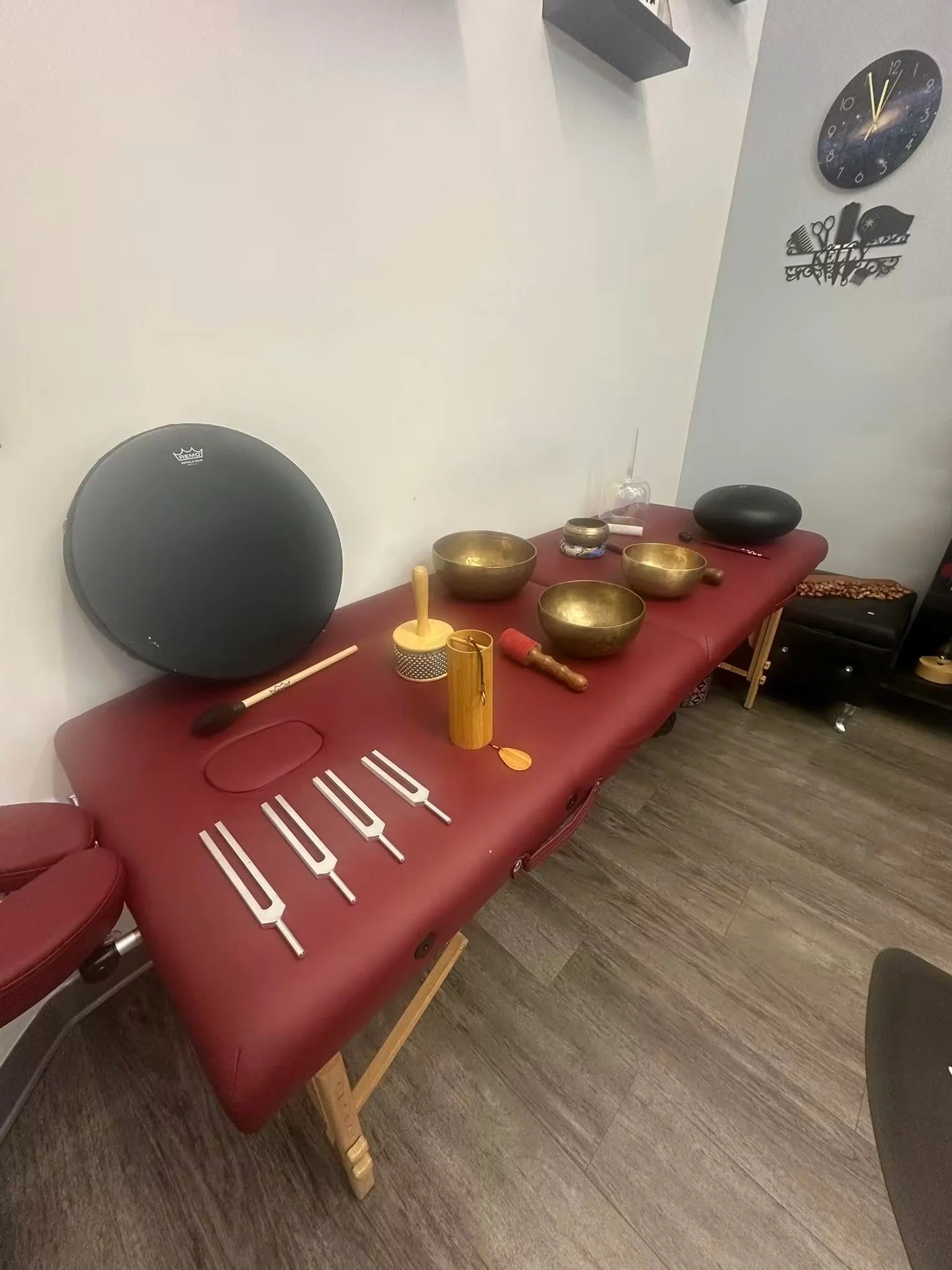 Sound healing treatment space with brass singing bowls, tuning forks, and mallets arranged on a massage table in a calm wellness studio.