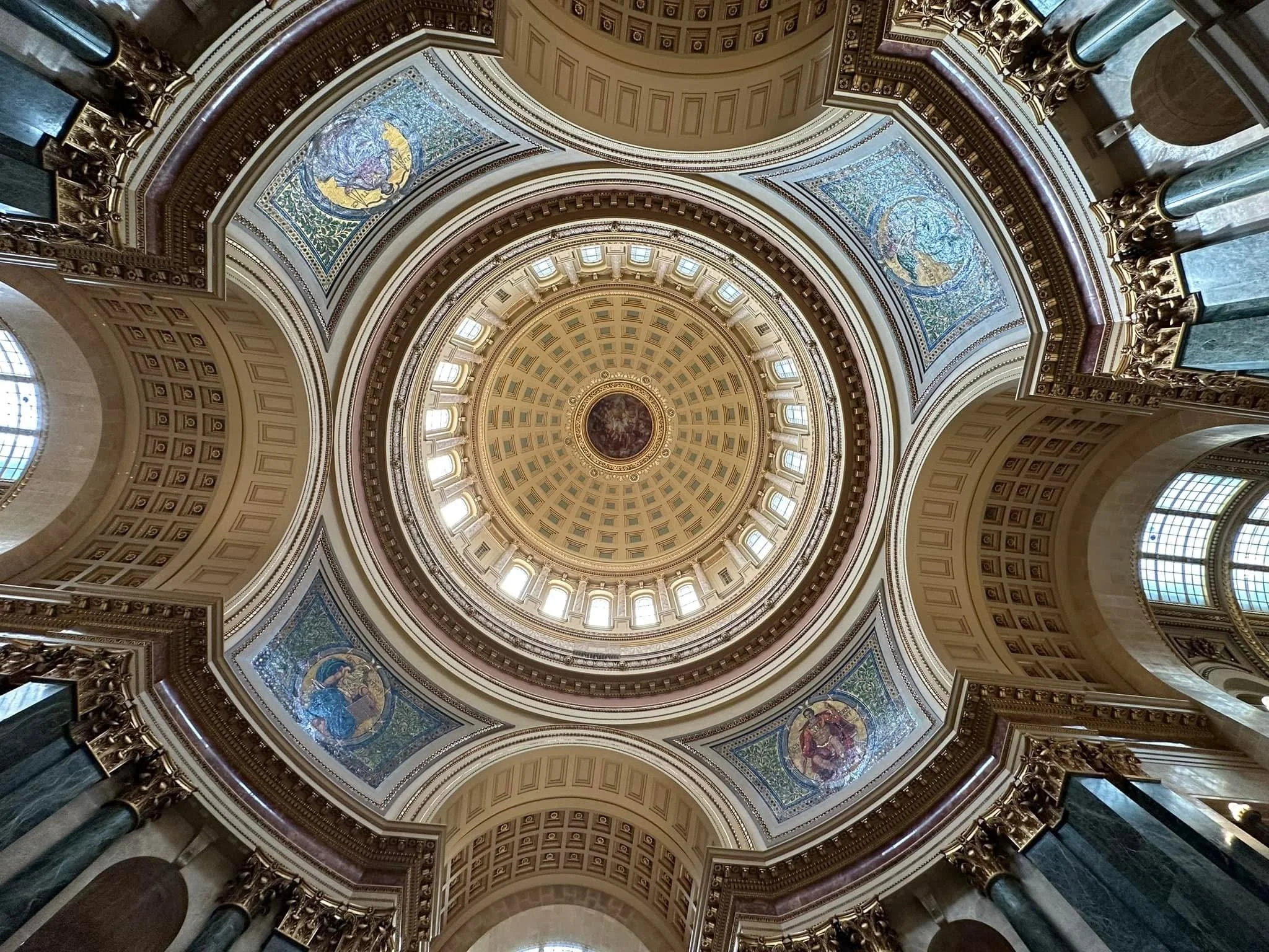 Photograph by Ashley Whitt looking up at the ornate rotunda dome inside the Wisconsin State Capitol in Madison, Wisconsin, featuring decorative gold accents, painted murals, and intricate architectural details.
