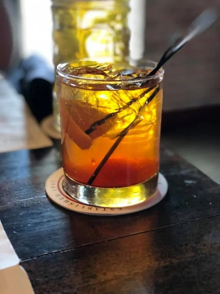 Photograph by Ashley Whitt of a Wisconsin brandy old fashioned served at WaterStreet Brewery in Oak Creek, Wisconsin, garnished with an orange slice and cherries in an old-fashioned glass on a dark wooden table.