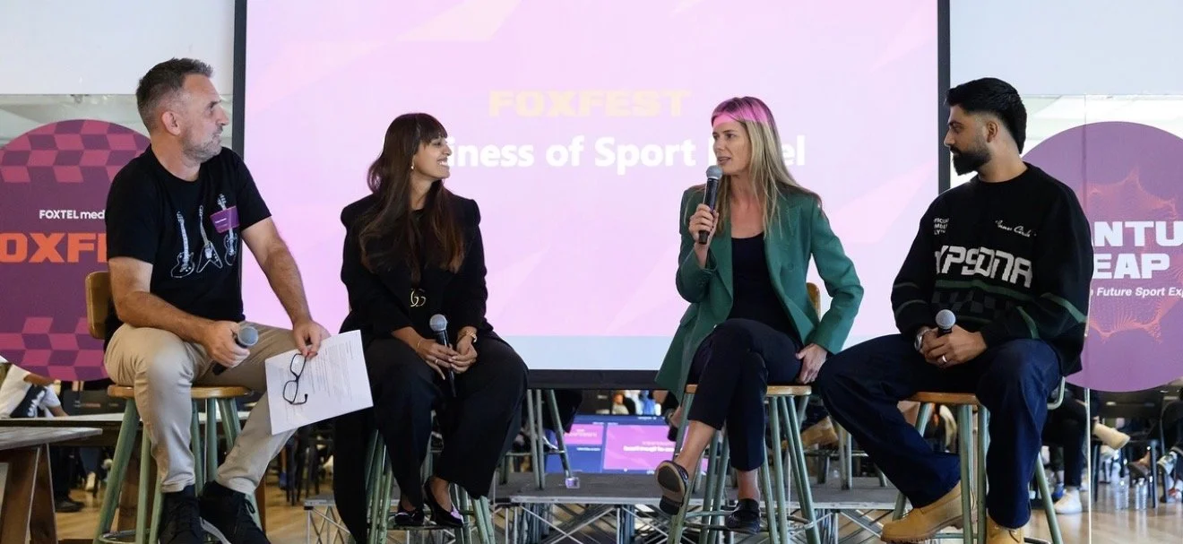 Four people sitting on stools on a stage, participating in a panel discussion at FOXFEST, with a large screen displaying the event name behind them.