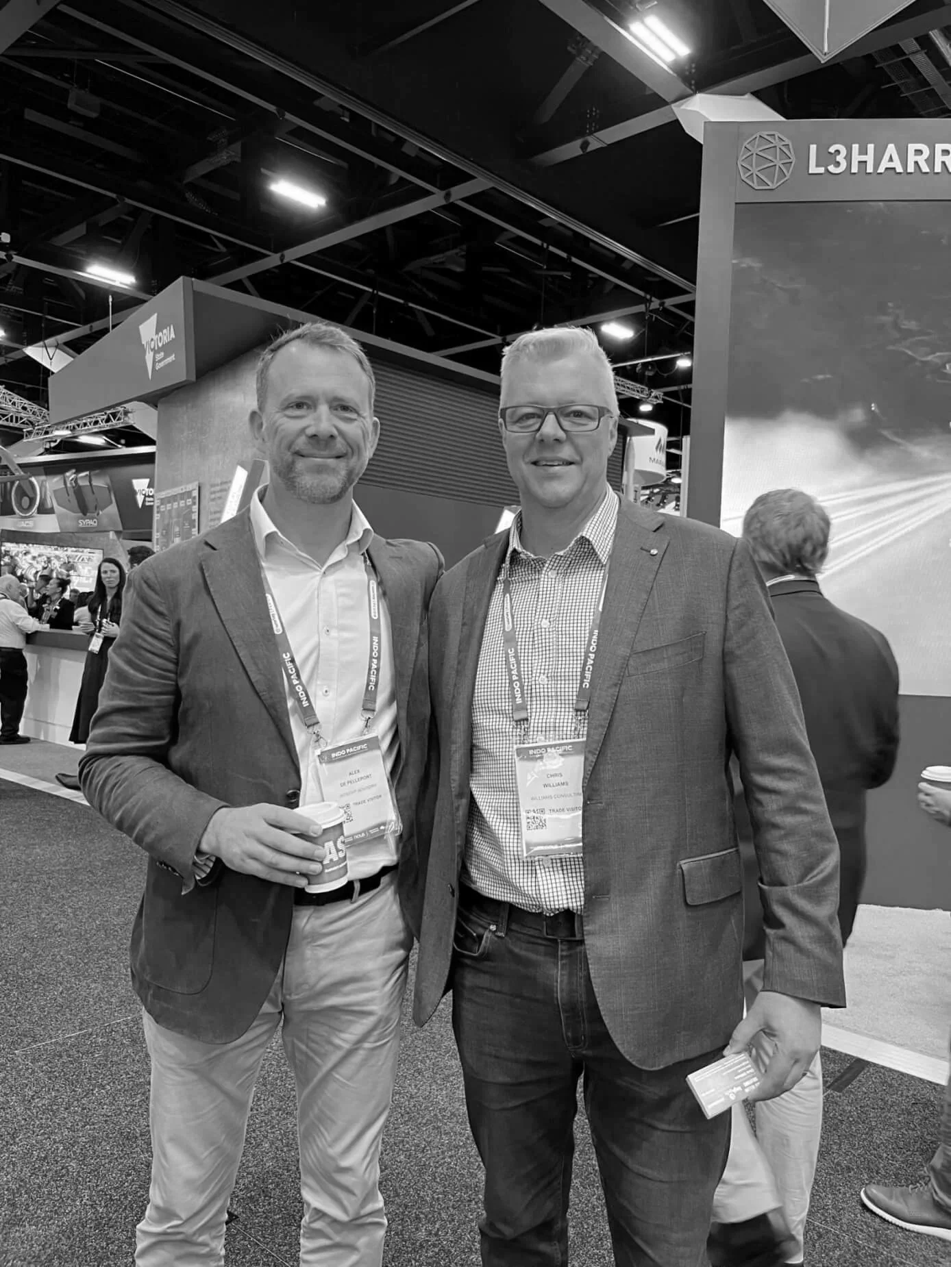 Black and white photo of Chris Williams and male colleague dressed in suits at a conference, standing close together with their arms around each other's shoulders, smiling at the camera.