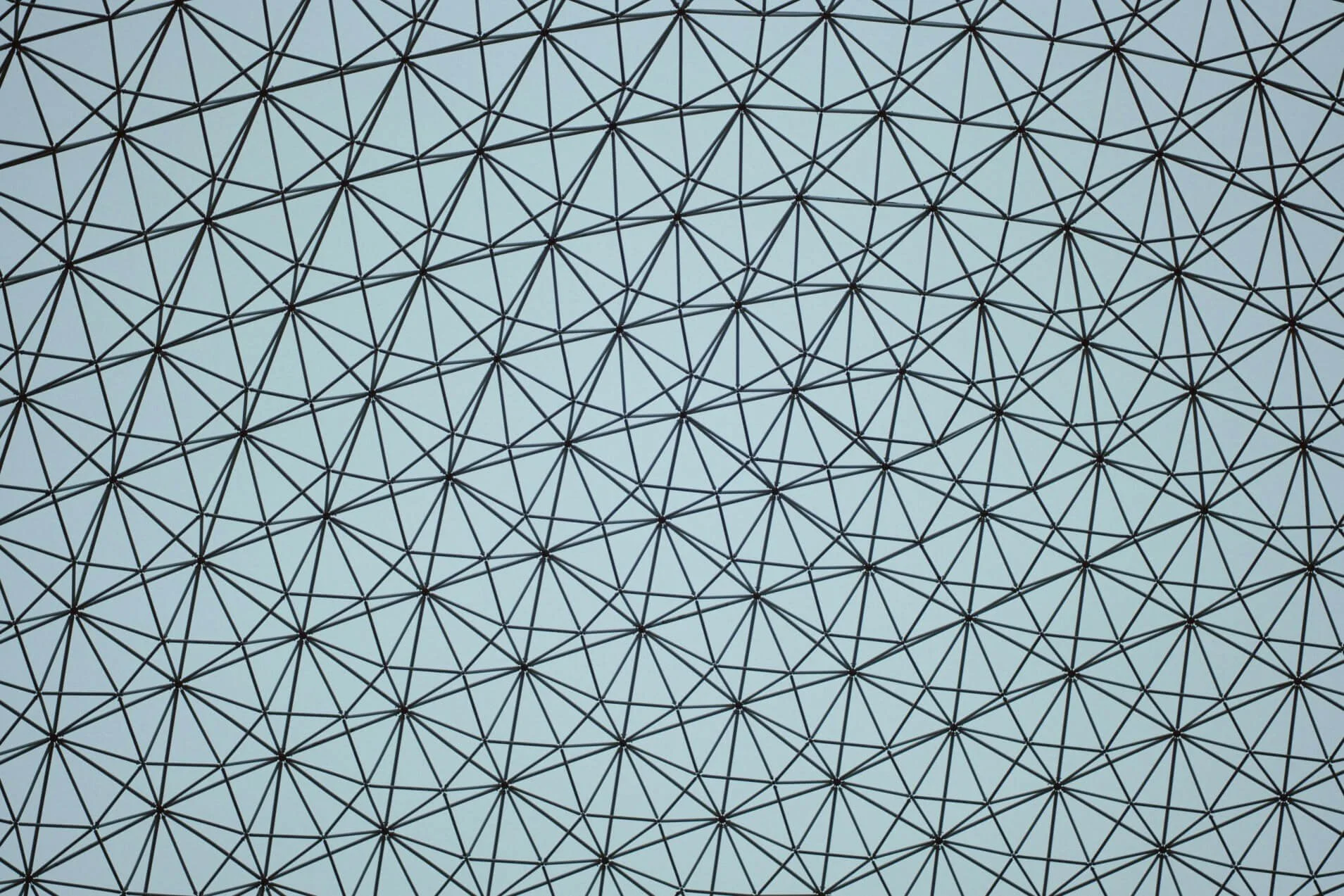 A large geodesic dome structure with a pattern of interconnected black metal rods against a cloudy sky.