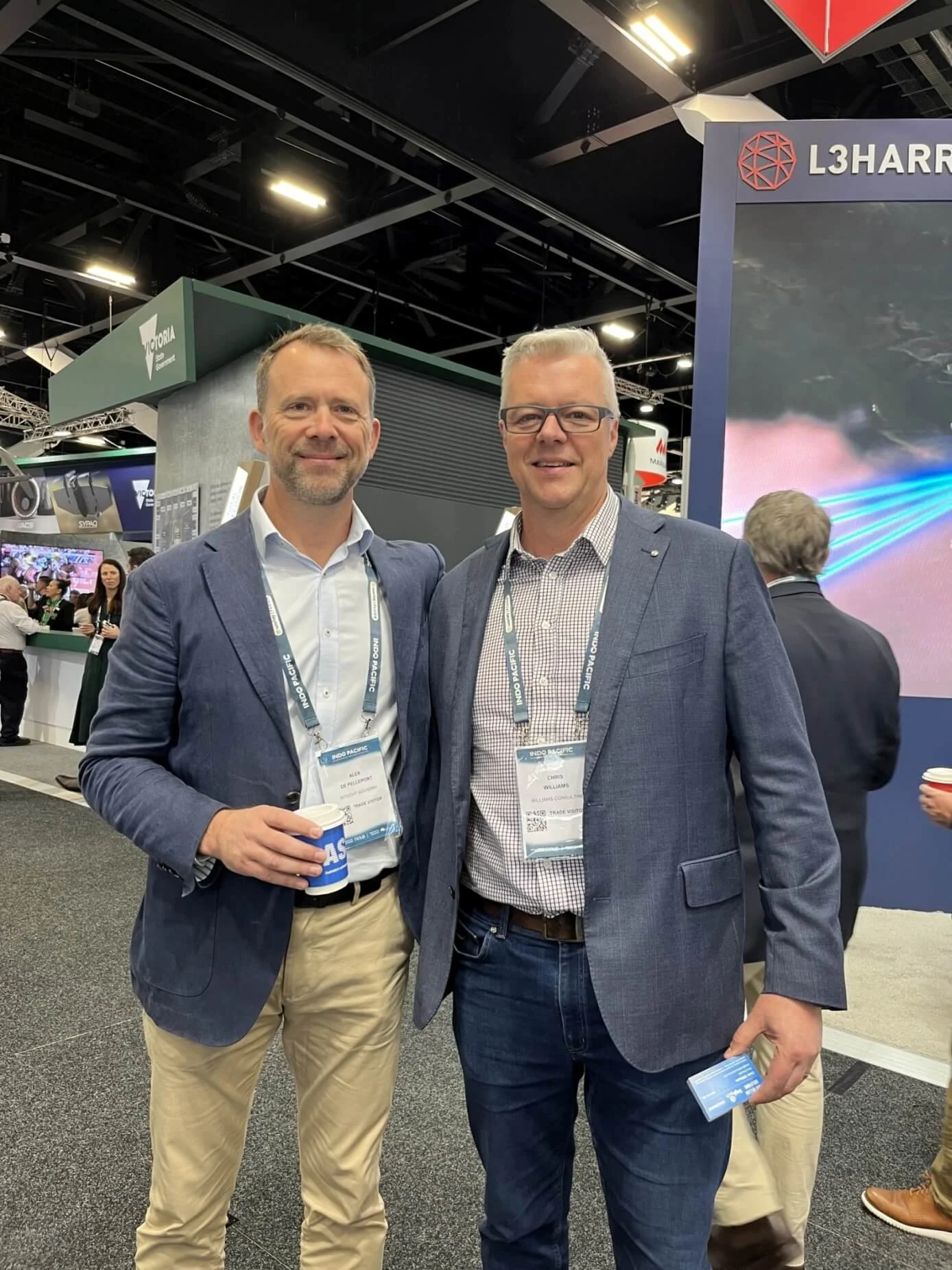 Colour photo of Chris Williams and male colleague dressed in suits at a conference, standing close together with their arms around each other's shoulders, smiling at the camera.