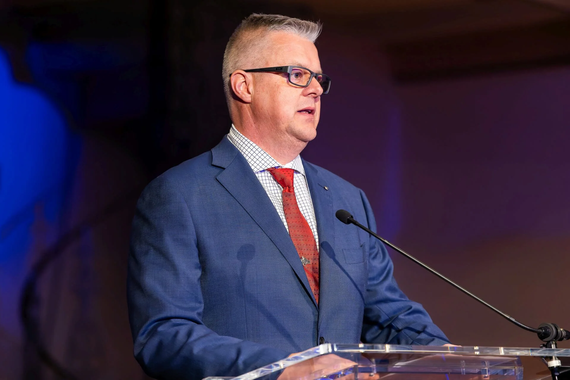 Colour photograph of Chris Williams speaking at a podium with a microphone.