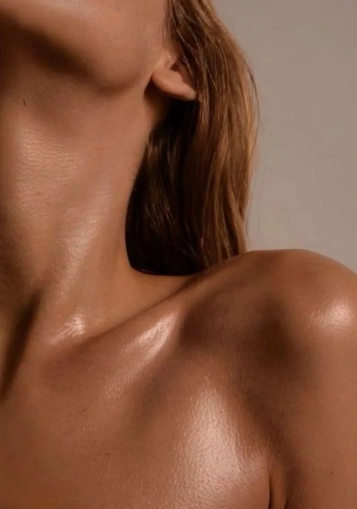 Close-up of a woman’s shoulder, part of her neck, and her hair, with a plain background.