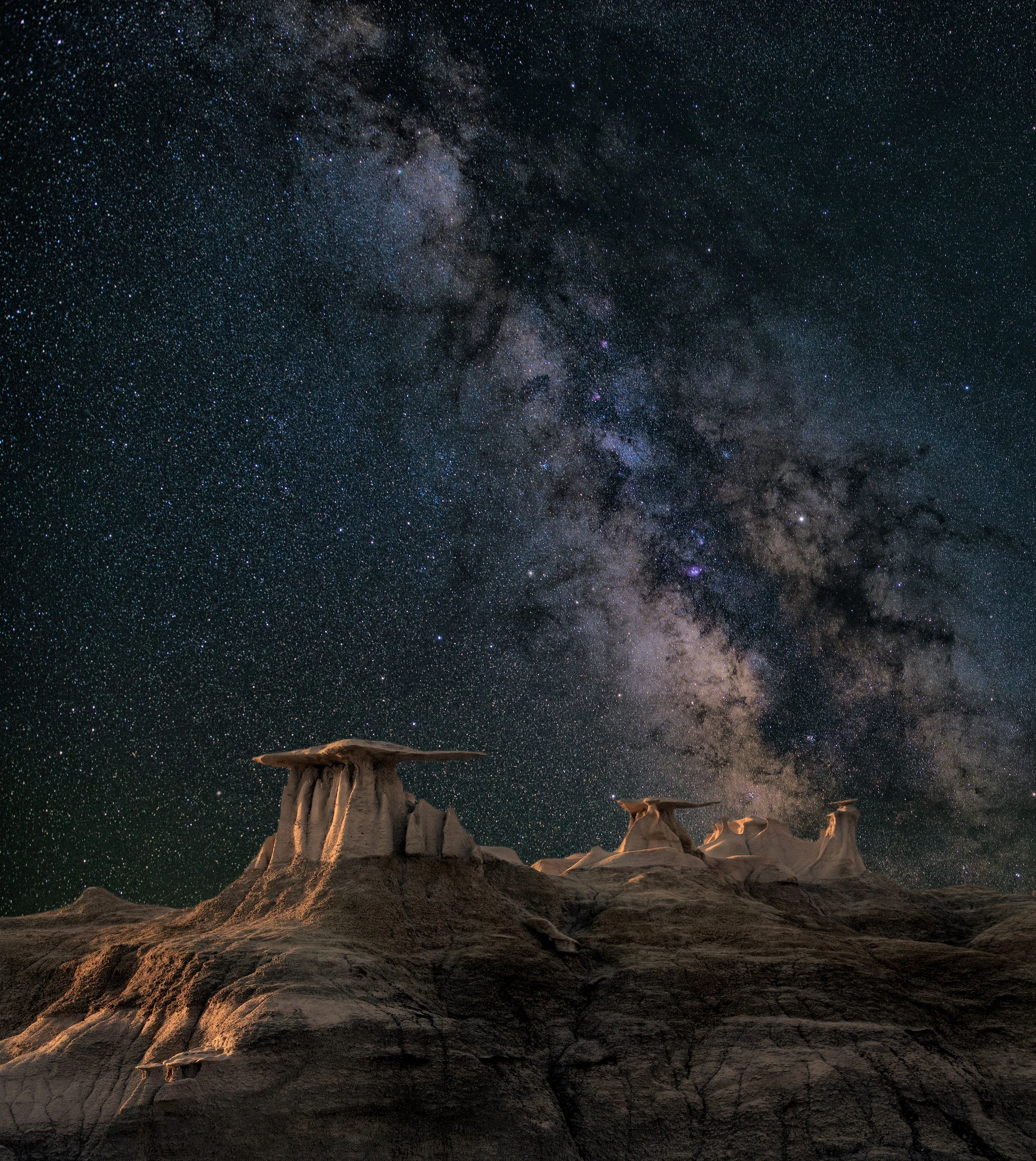 Night sky filled with countless stars and the Milky Way galaxy, viewed from a desert landscape with unique rock formations.