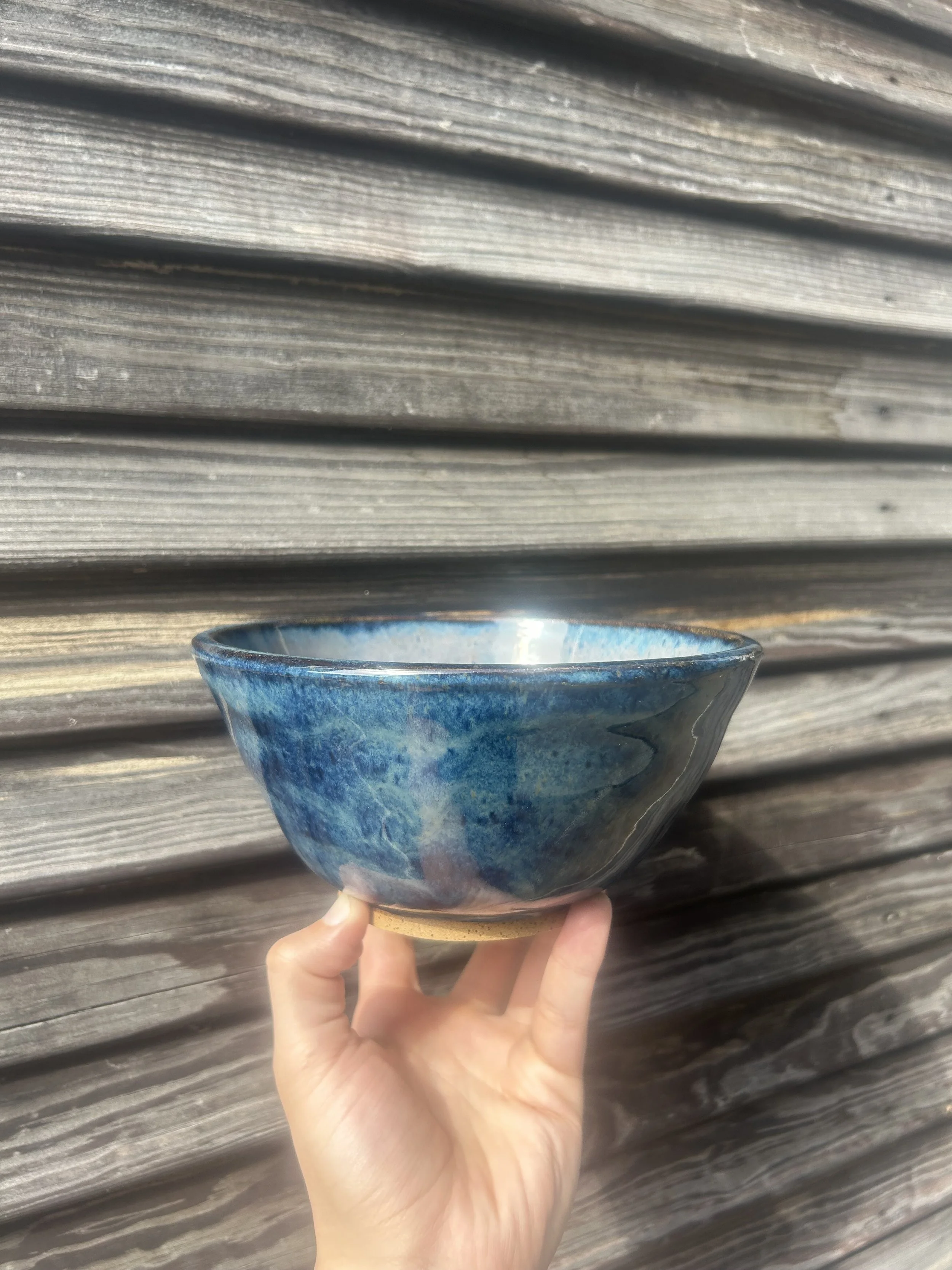 A hand holds a blue and brown ceramic bowl with a wooden textured background.