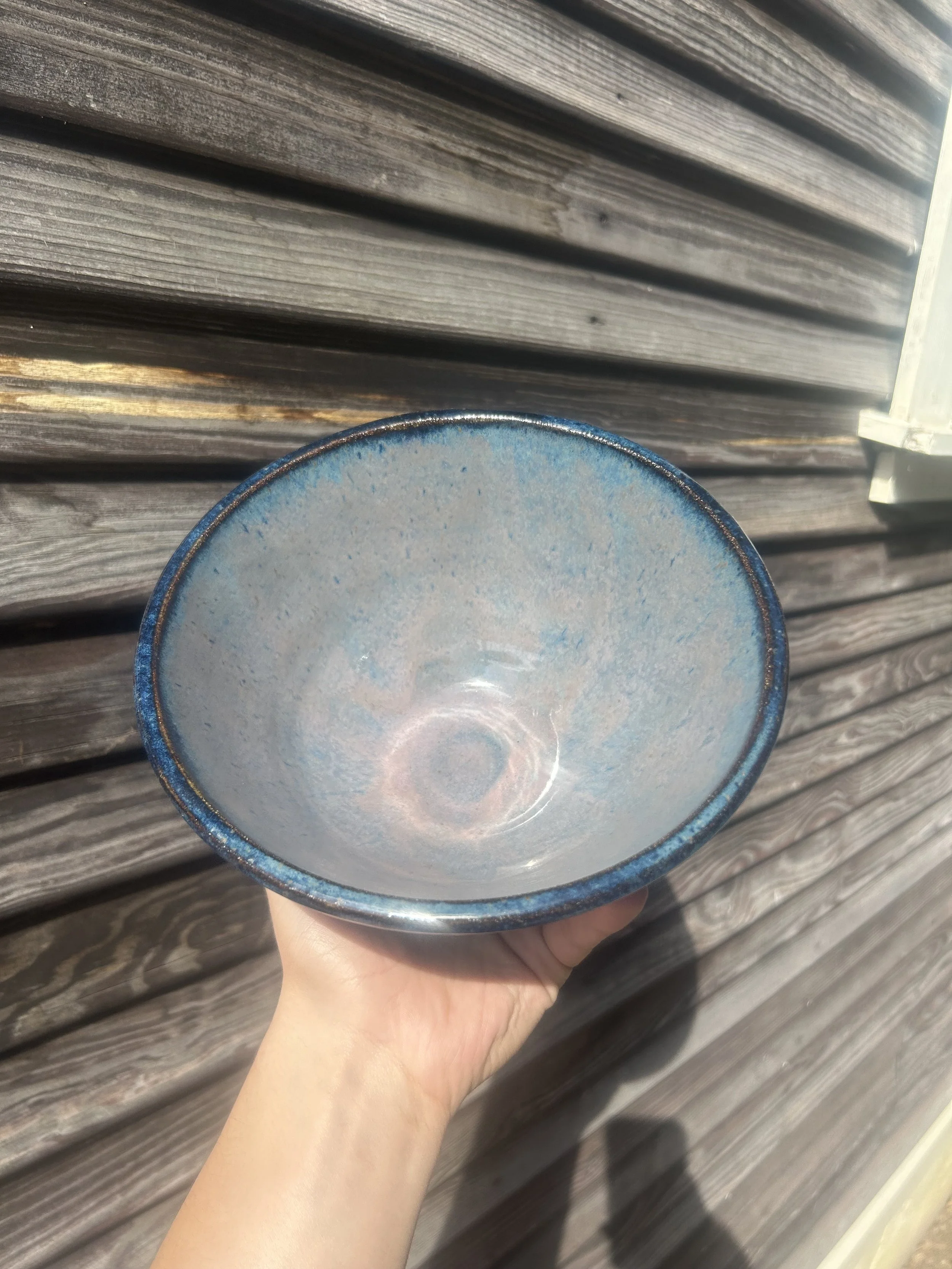 A person holding a blue and white ceramic cup against a wooden background, showing the underside of the cup.