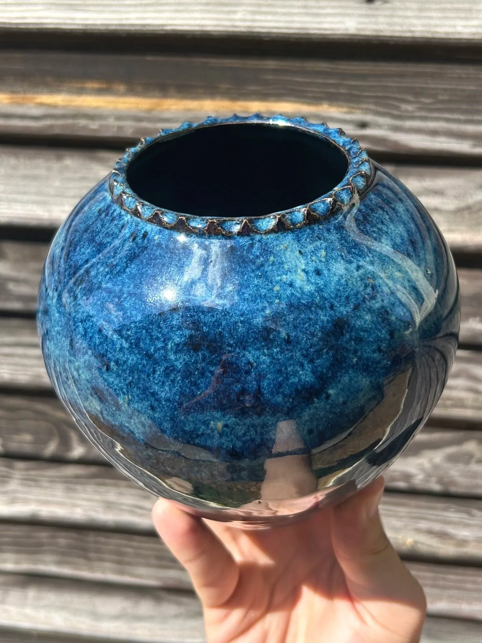 A hand holding a blue glass vase with a glossy, marbled pattern, set against a wooden background.