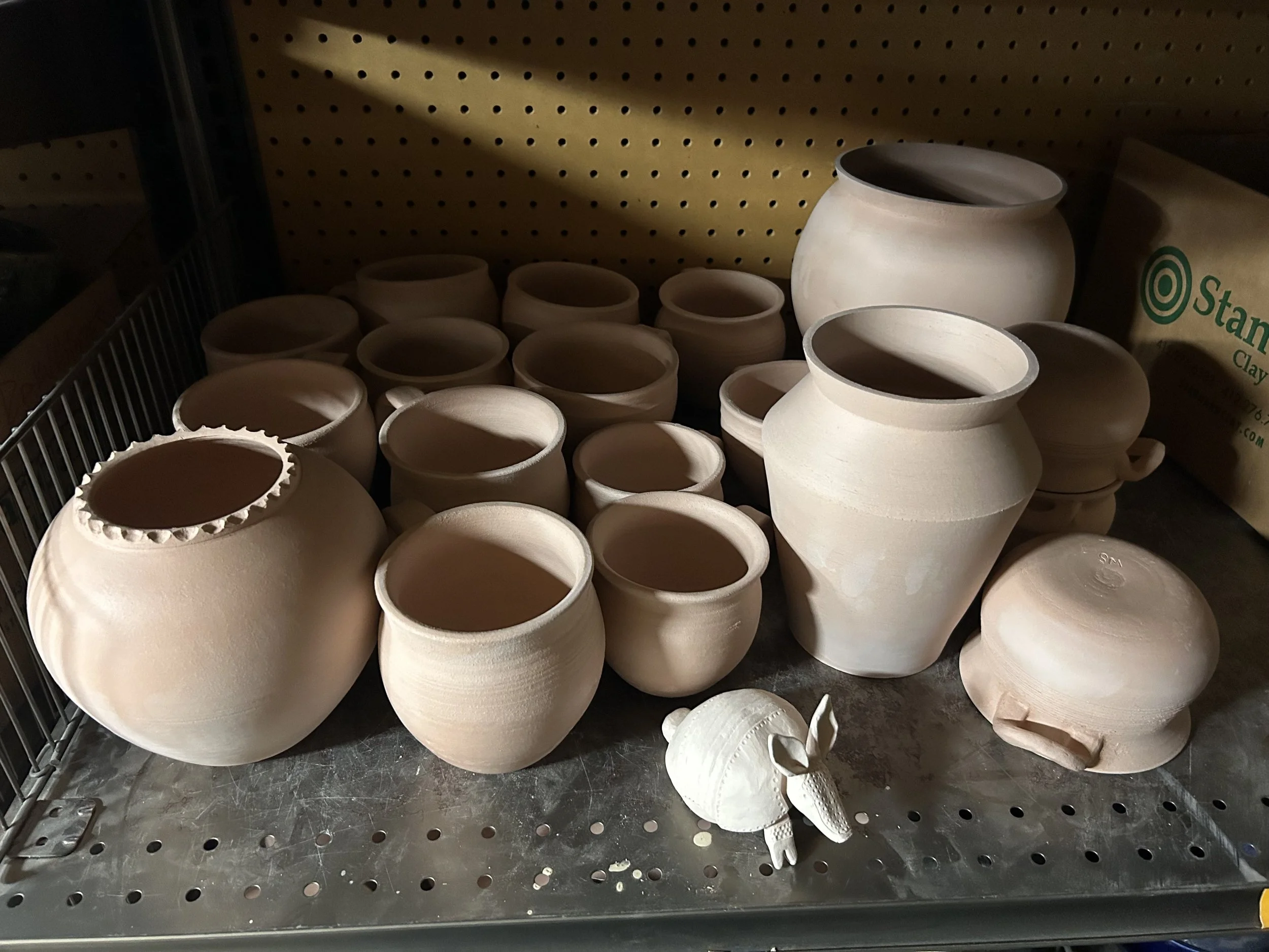 Unfinished ceramic pots on a metal shelf in a pottery studio